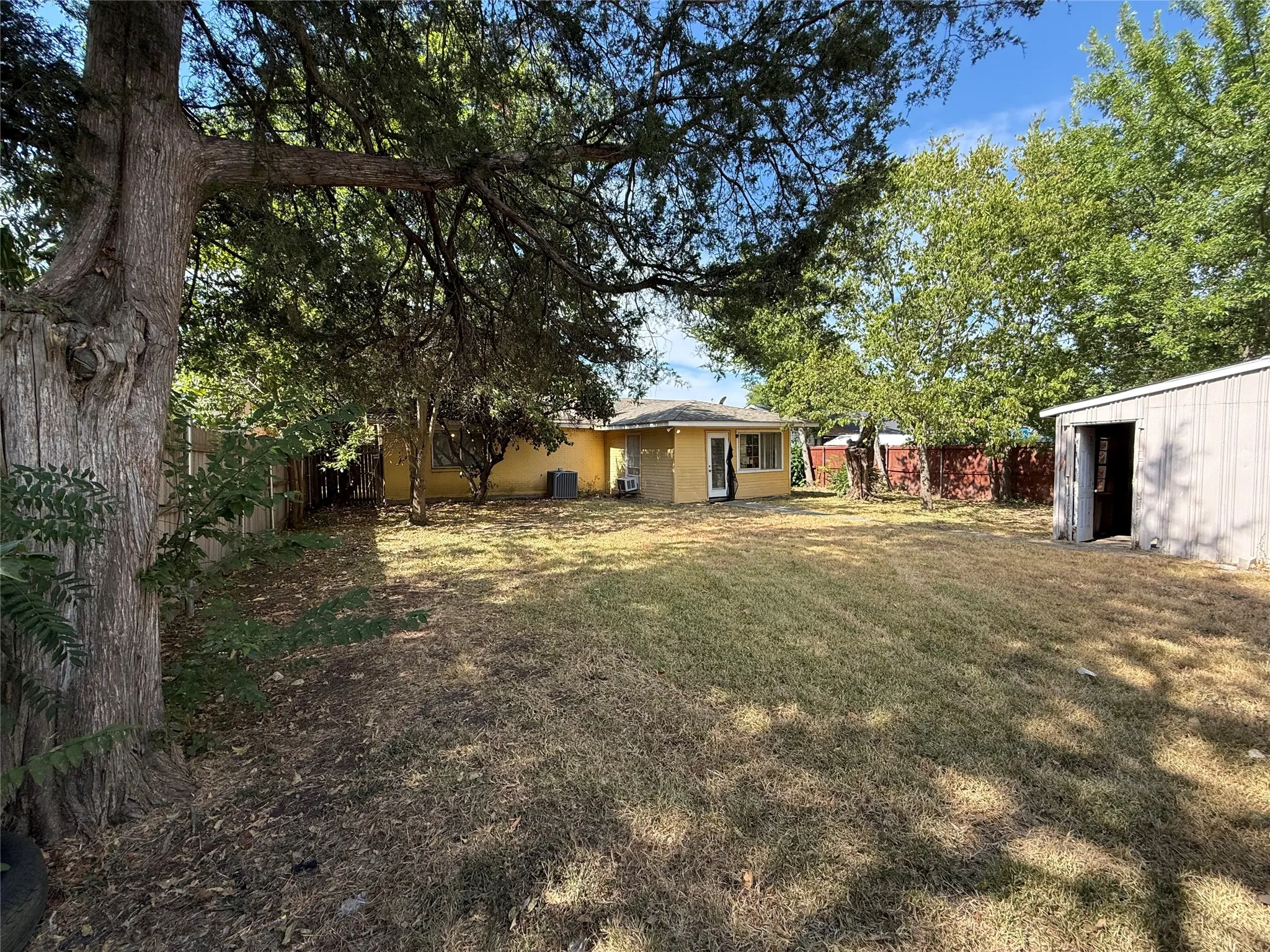 Expansive backyard with a storage shed, mature trees, and a yellow exterior property