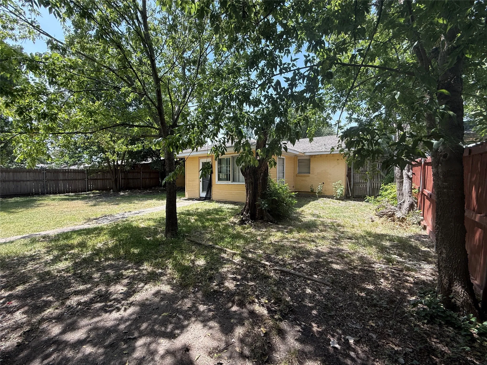 Expansive backyard featuring a fenced perimeter, mature trees, and a stucco exterior