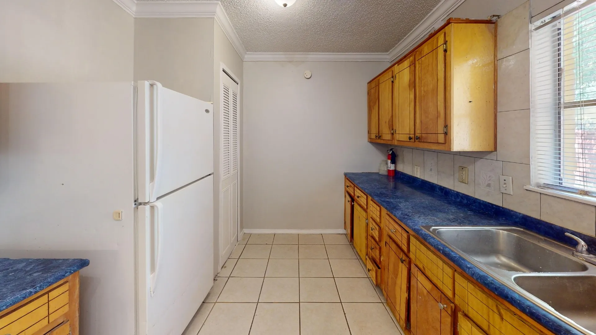 Kitchen with wood cabinetry, blue countertops, tile flooring, and a double basin stainless steel sink