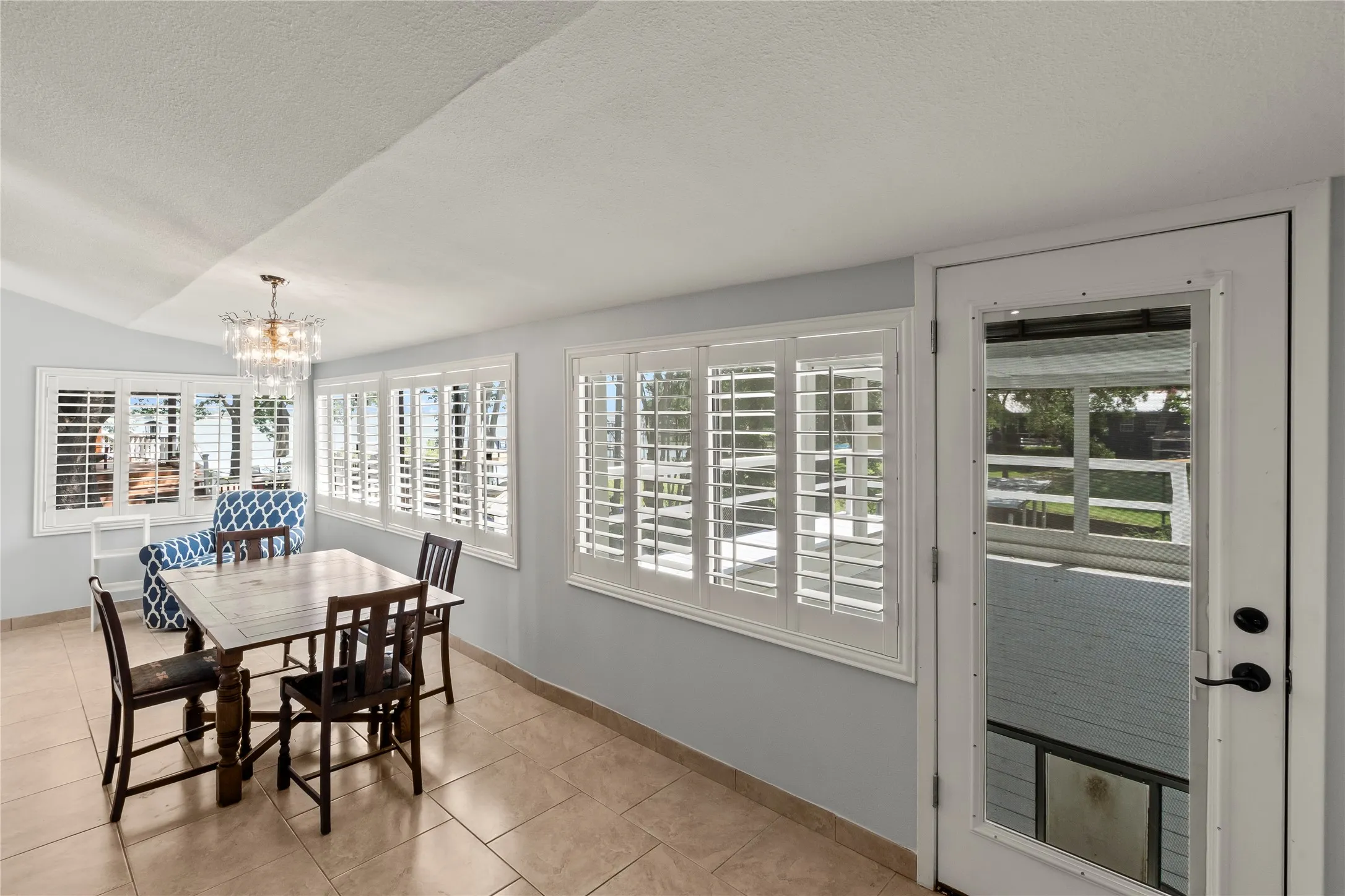 Recessed ceiling, transom window, multiple windows with plantation shutters, tile flooring, and a glass-paneled door