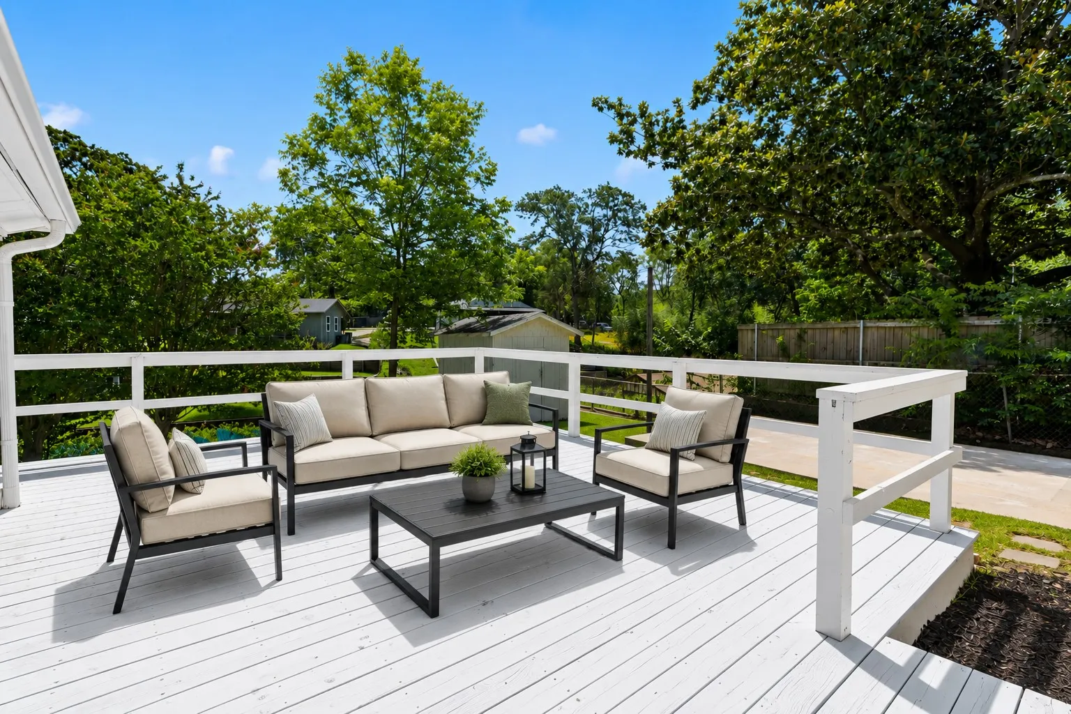 Spacious outdoor deck with white railing, featuring a solid surface, and surrounded by mature trees