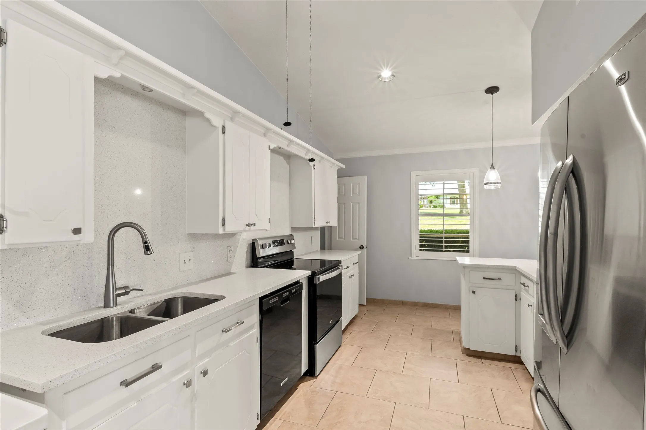 White cabinetry with decorative molding, dual basin stainless steel sink with gooseneck faucet, light-toned tile flooring, and stainless steel appliances