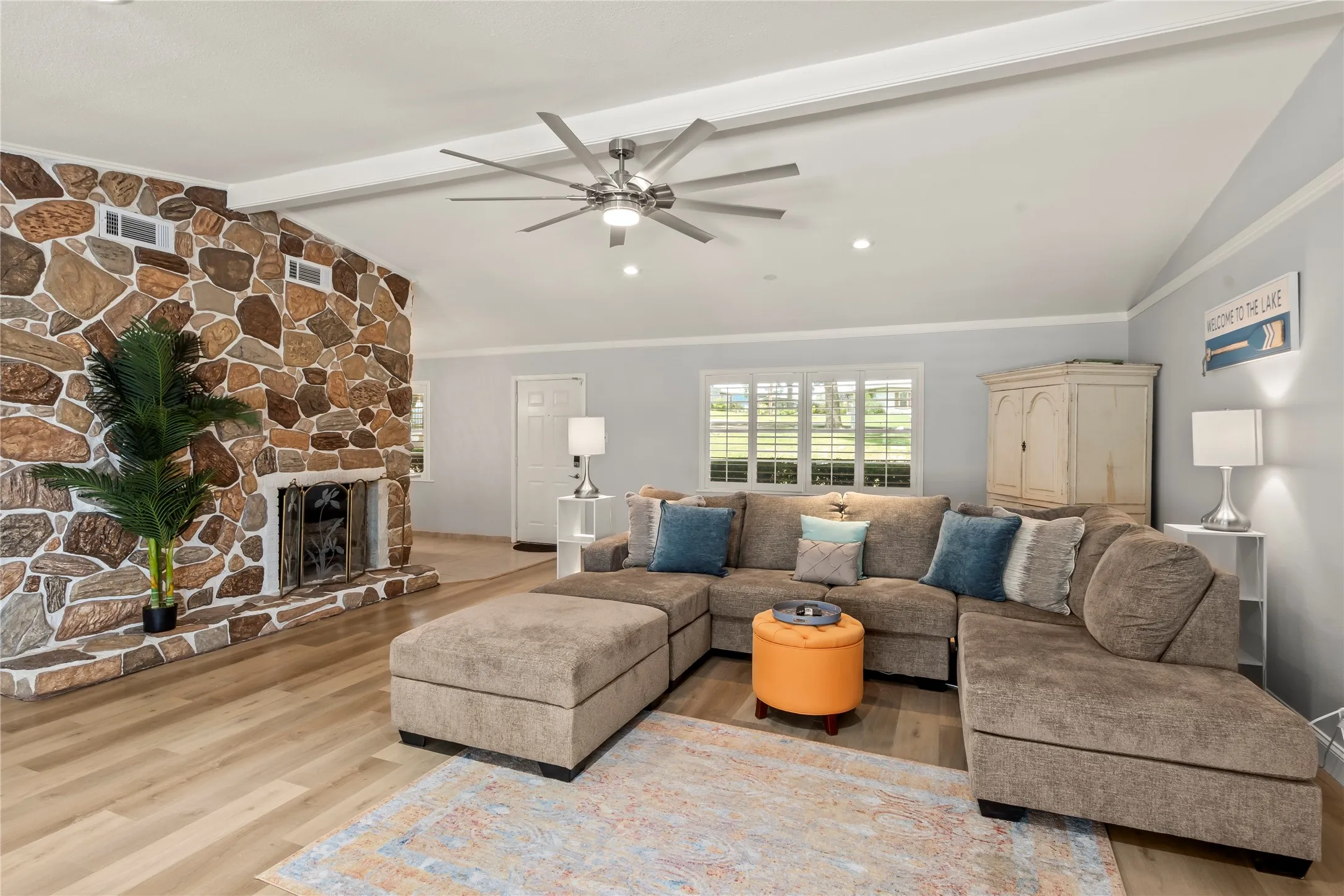 Vaulted ceiling, stone-clad fireplace, wood-finish flooring, recessed lighting, and a ceiling fan