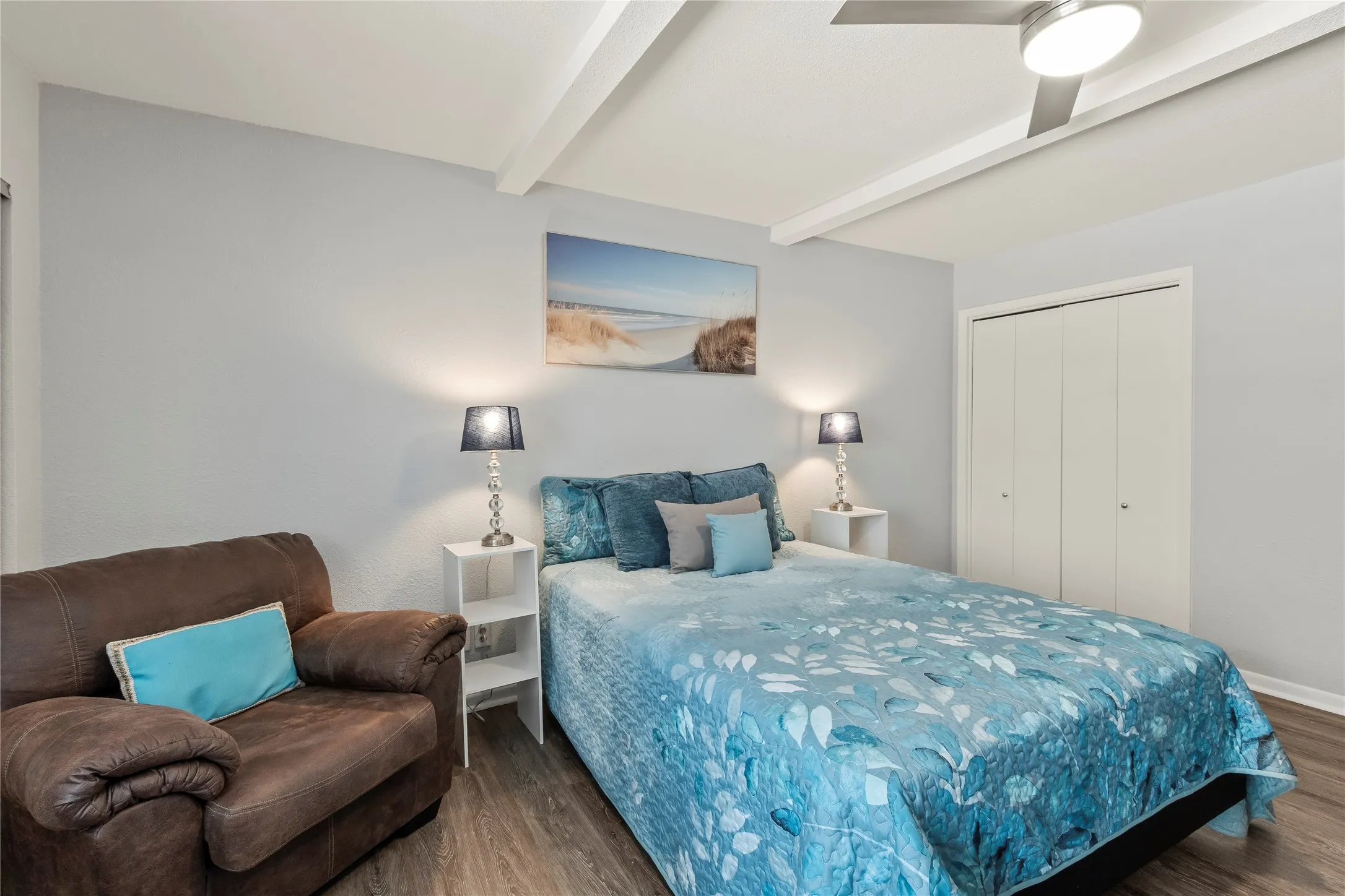 Wood-finish flooring, ceiling fan, white bi-fold closet doors, and exposed ceiling beams
