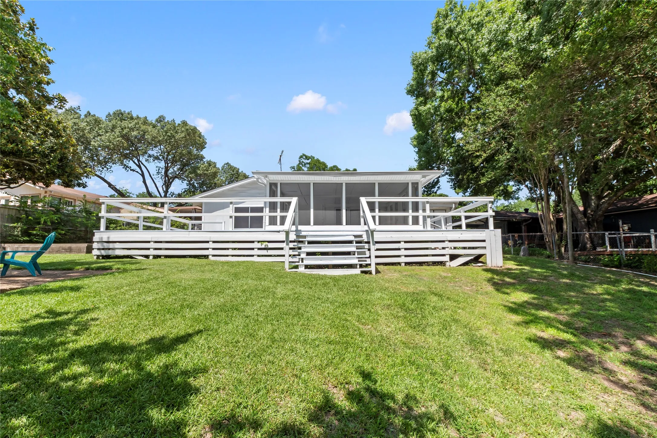 Spacious rear yard with a sloped lawn, a large wood deck with railings, and a screened-in porch