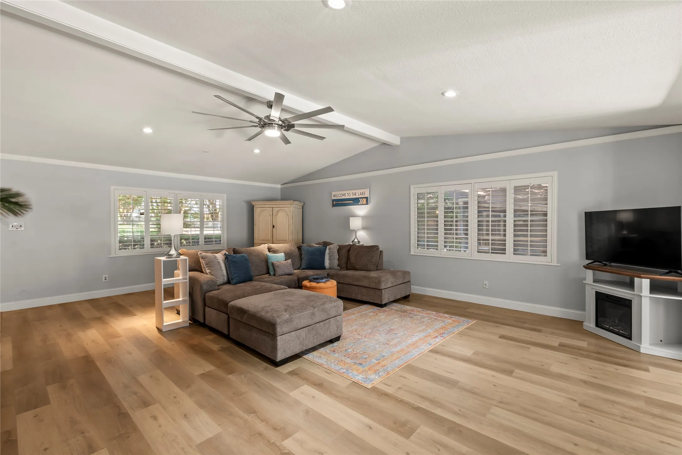 Vaulted ceiling with exposed beam, recessed lighting, wood-finish flooring, and window shutters