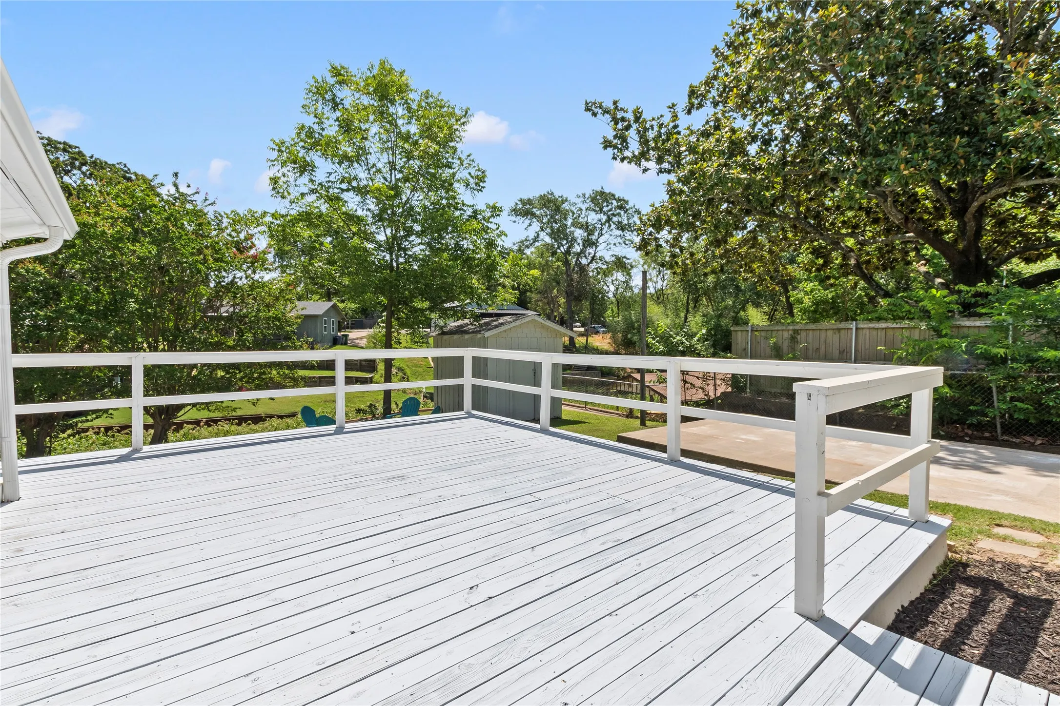 Expansive wooden deck with white railing, overlooking a lush green yard with mature trees