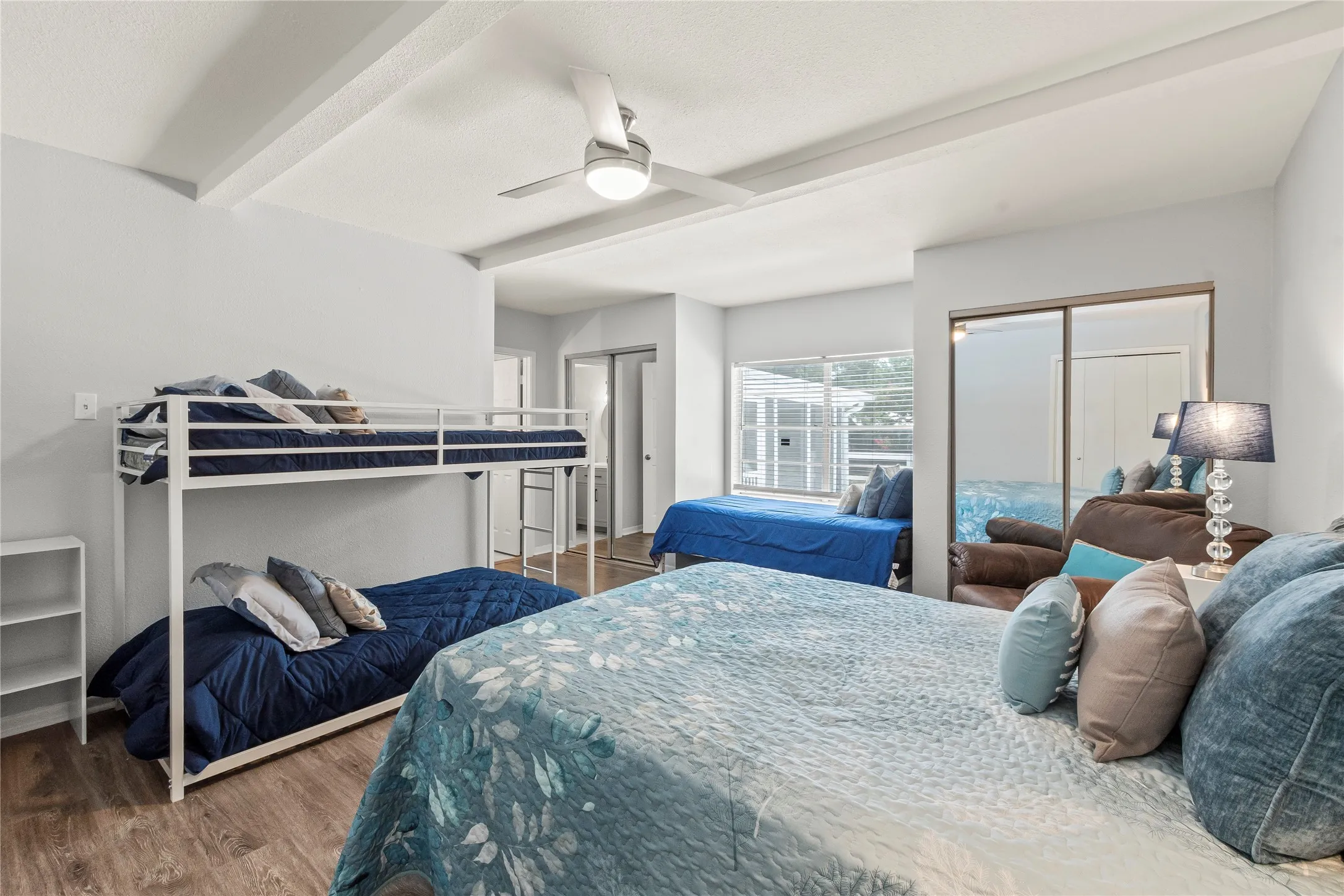 Recessed ceiling with exposed beams, wood-finish flooring, ceiling fan with integrated lighting, mirrored sliding closet doors, and window with horizontal blinds