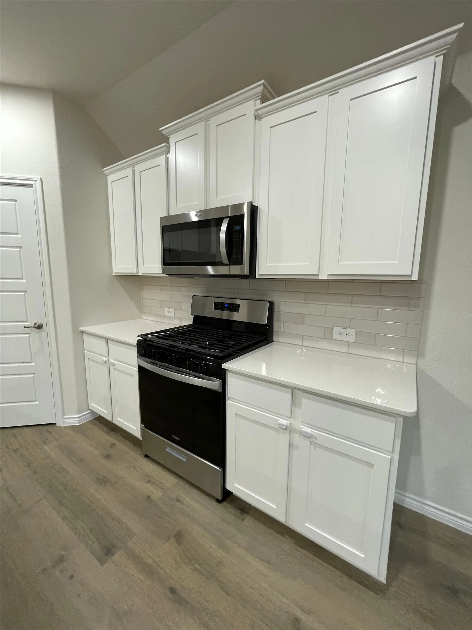 Kitchen featuring stainless steel appliances, dark wood-style floors, white cabinetry, tasteful backsplash, and lofted ceiling