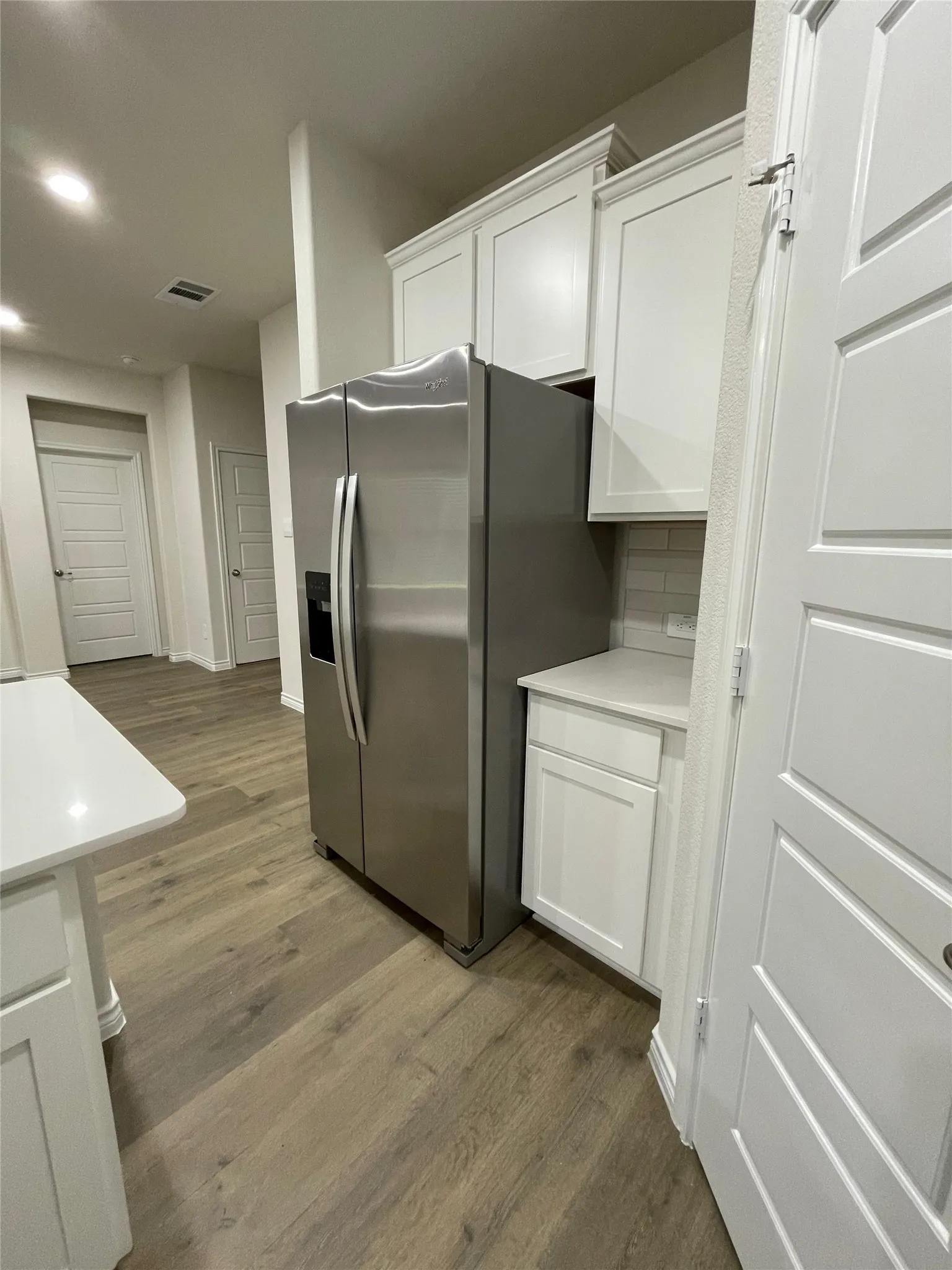 Kitchen with wood finished floors, stainless steel refrigerator with ice dispenser, white cabinets, light countertops, and recessed lighting