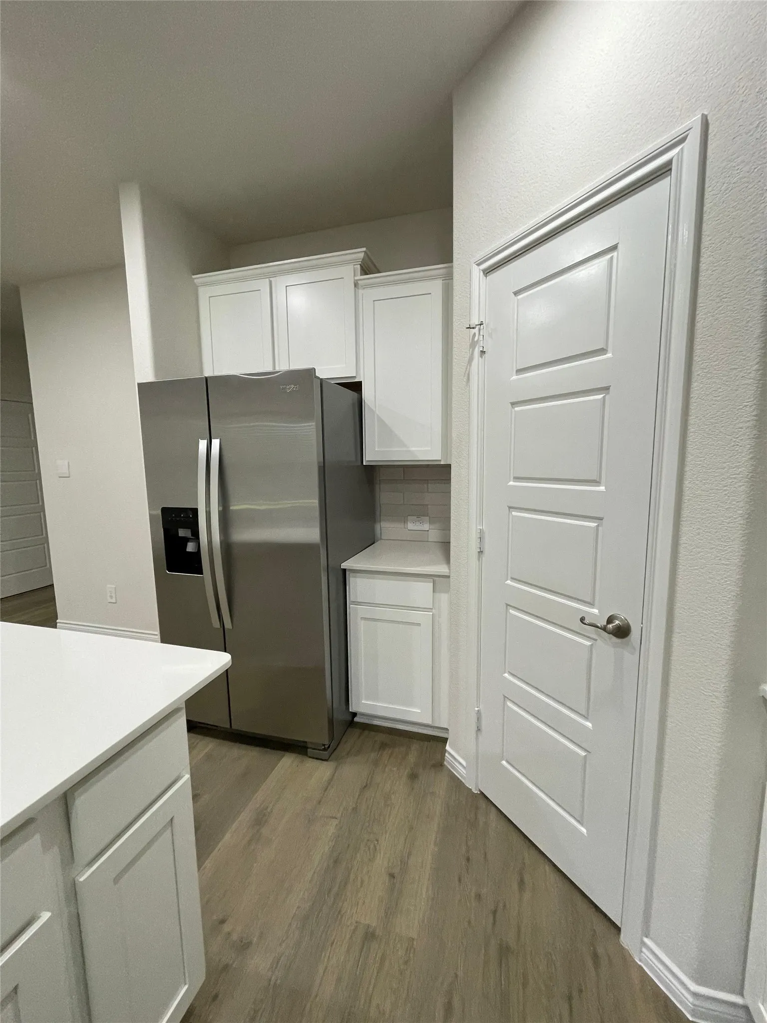 Kitchen with stainless steel fridge with ice dispenser, wood finished floors, light countertops, and white cabinetry