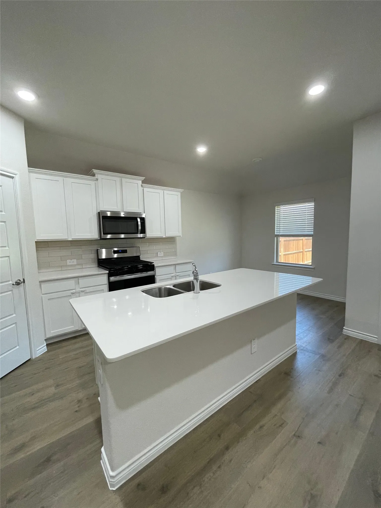 Kitchen featuring stainless steel appliances, a center island with sink, tasteful backsplash, white cabinets, and dark wood finished floors
