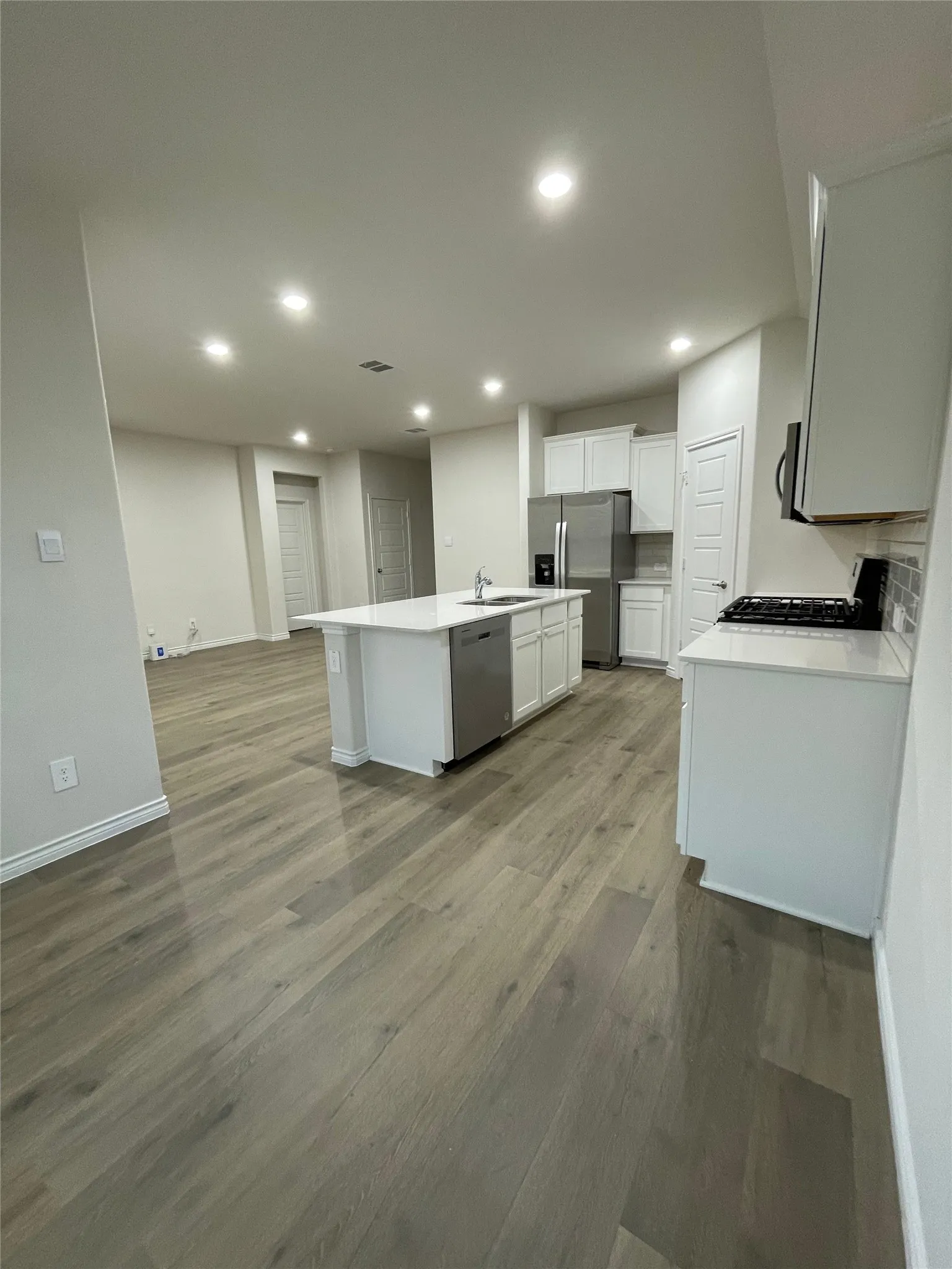 Kitchen with an island with sink, wood finished floors, stainless steel appliances, white cabinets, and recessed lighting