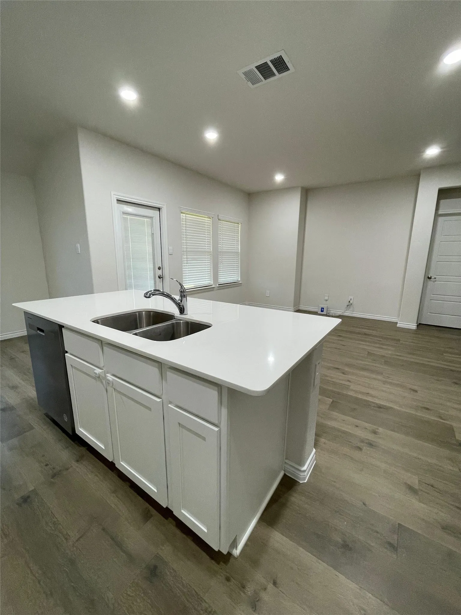 Kitchen featuring a kitchen island with sink, dark wood-style flooring, white cabinets, dishwasher, and light countertops