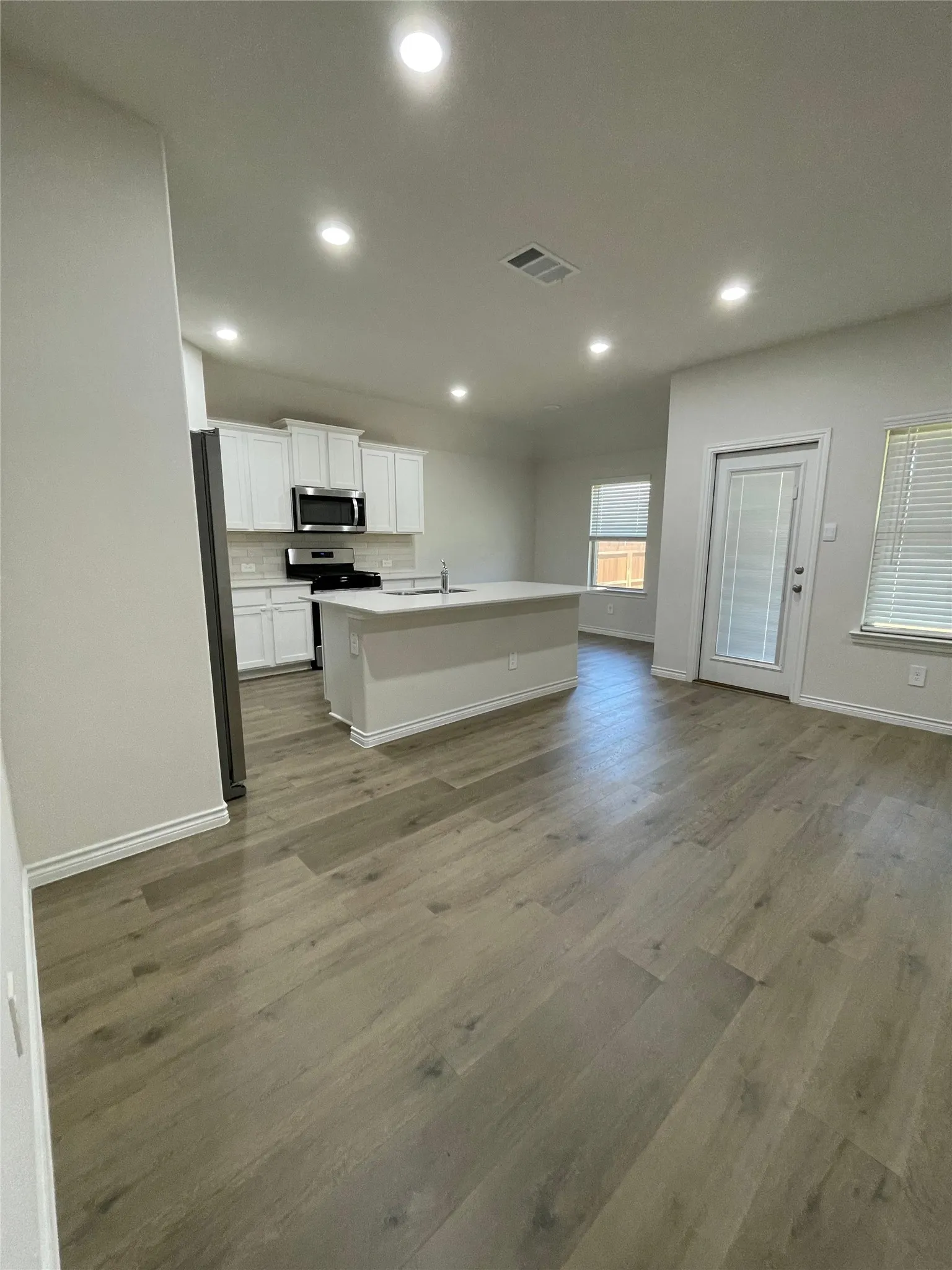 Kitchen with open floor plan, wood finished floors, stainless steel appliances, an island with sink, and white cabinets