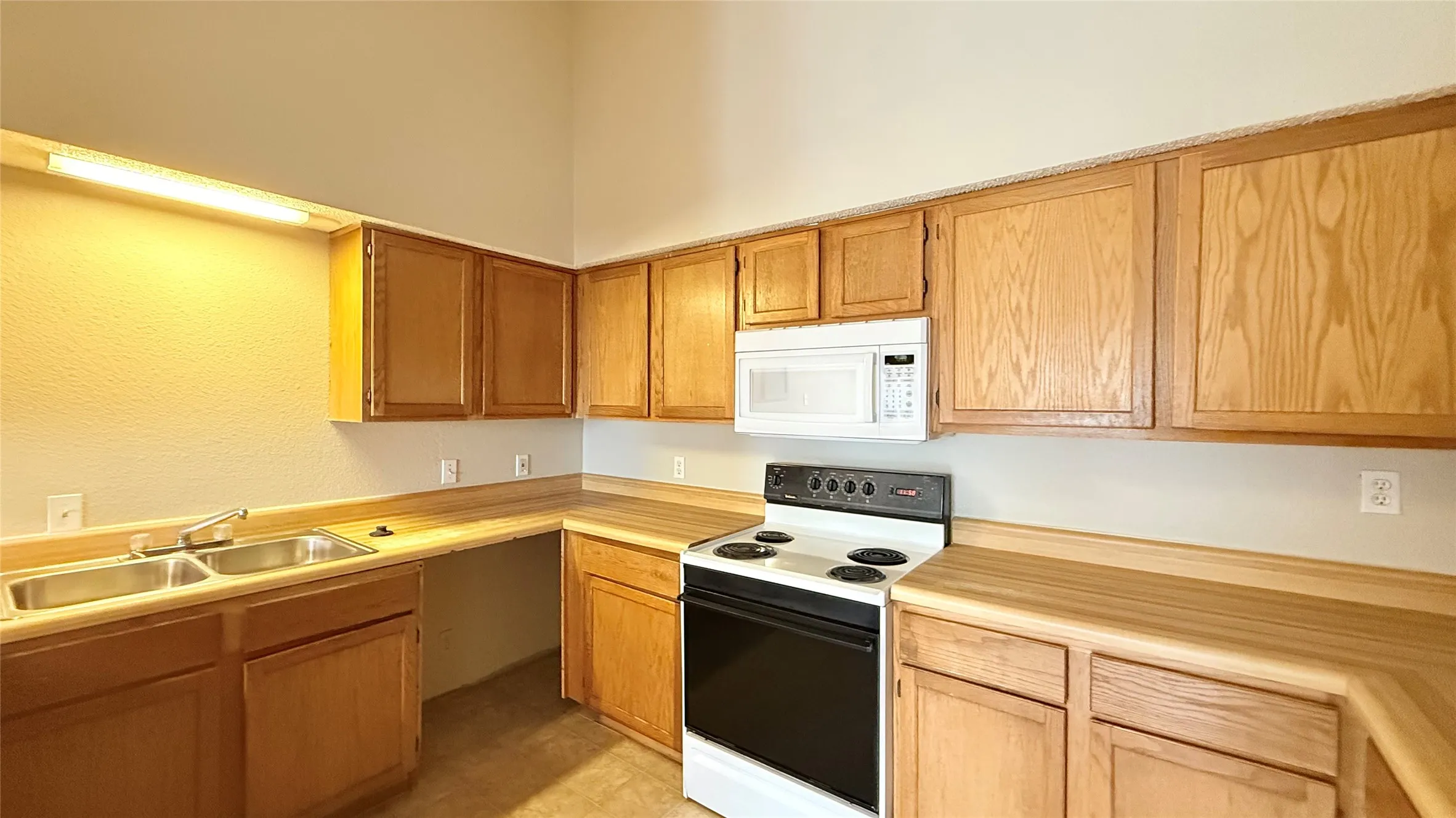 Kitchen featuring wood-finish cabinetry, a double basin stainless steel sink, a microwave, and a range oven