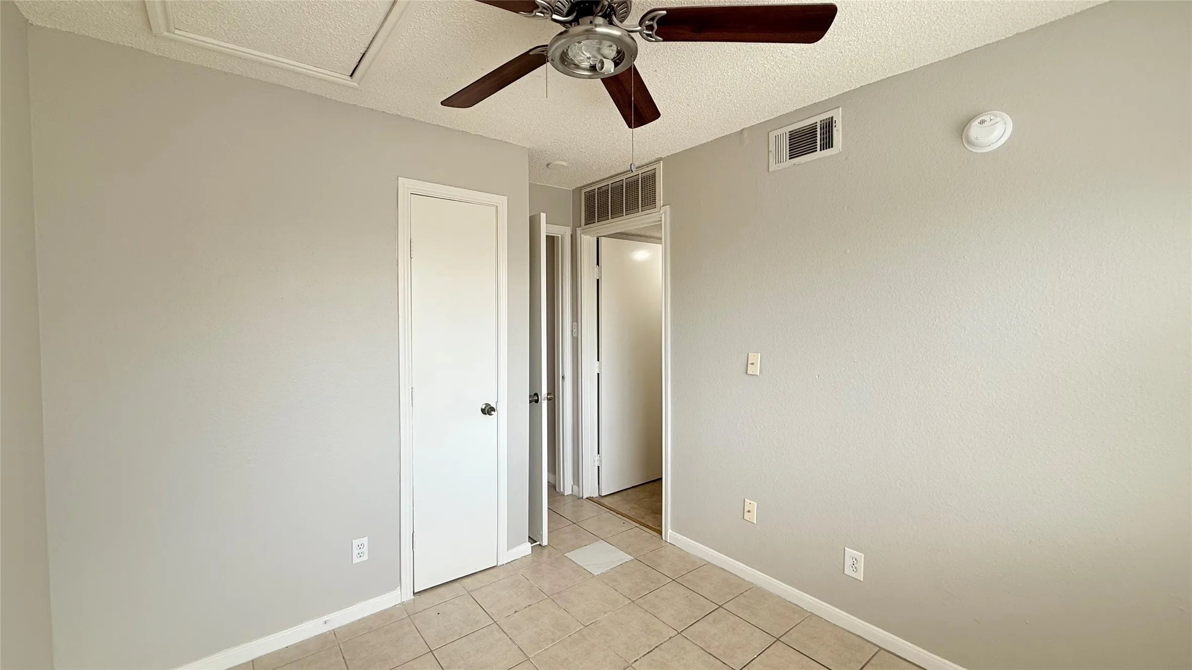 Ceiling fan with wood-finish blades, light gray painted walls, and square tile flooring