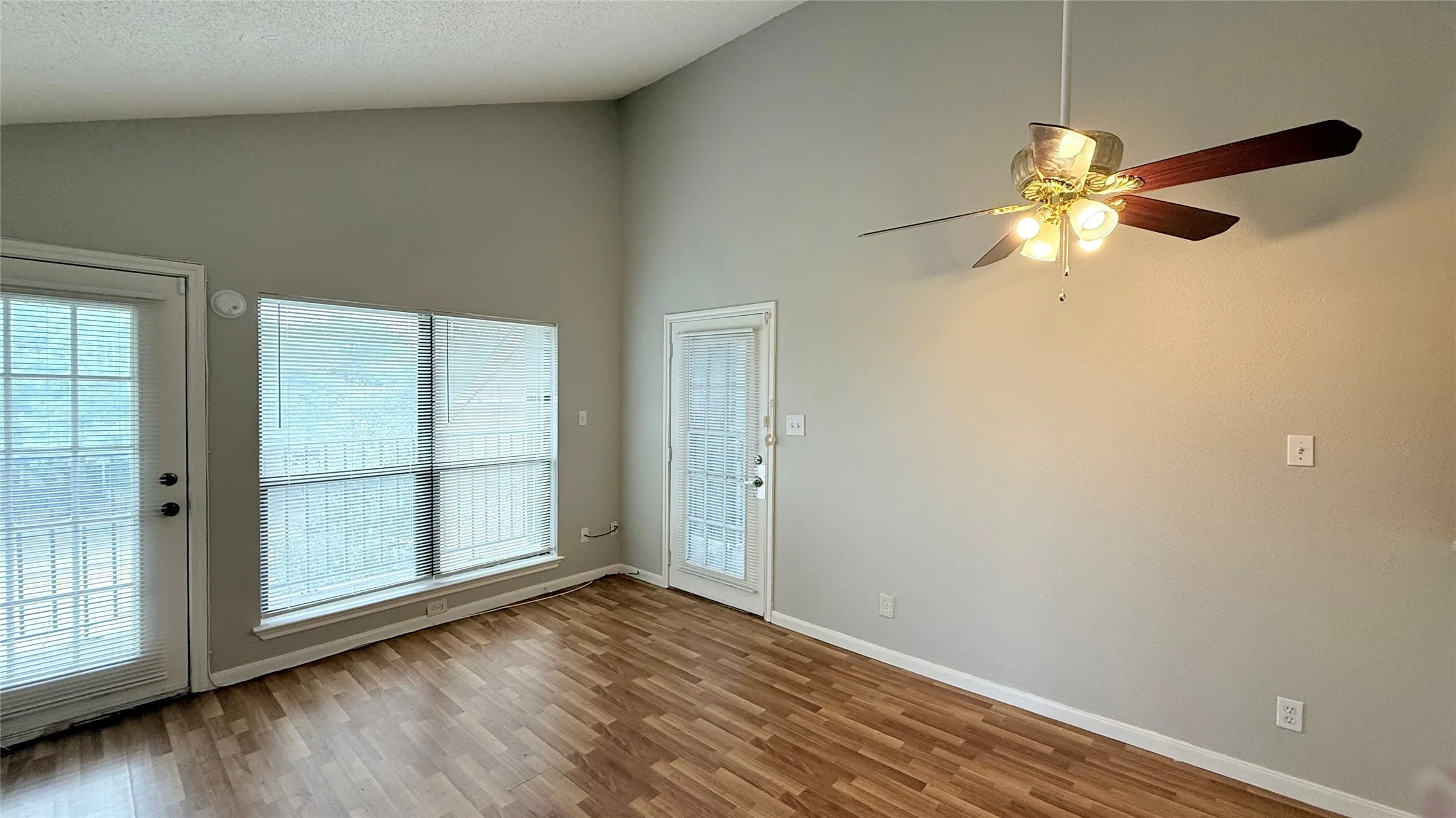 Vaulted ceilings, wood-finish flooring, two glass-paned doors, and a ceiling fan with integrated lighting