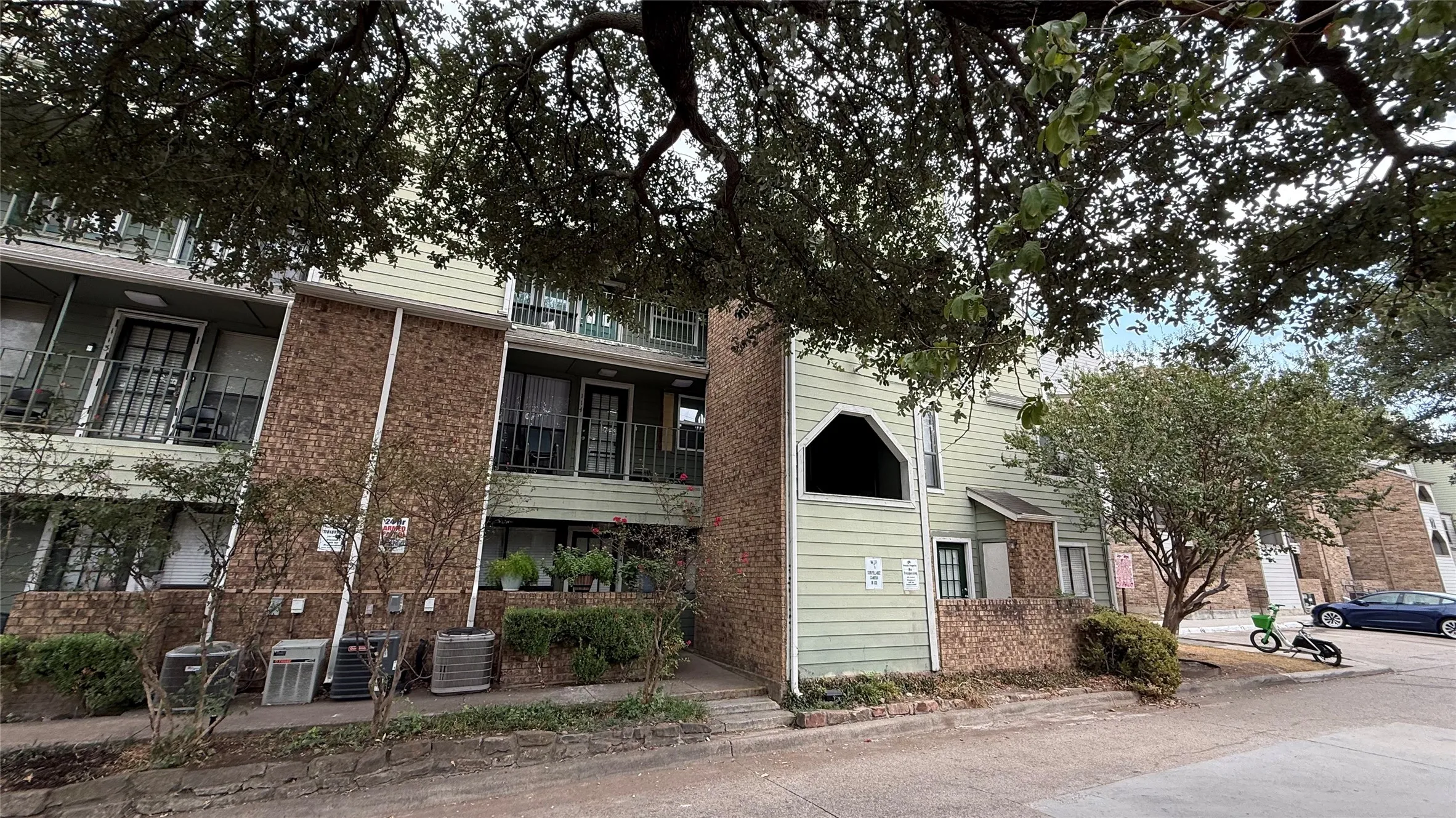 Brick and siding exterior with multiple balconies, featuring mature trees and established landscaping