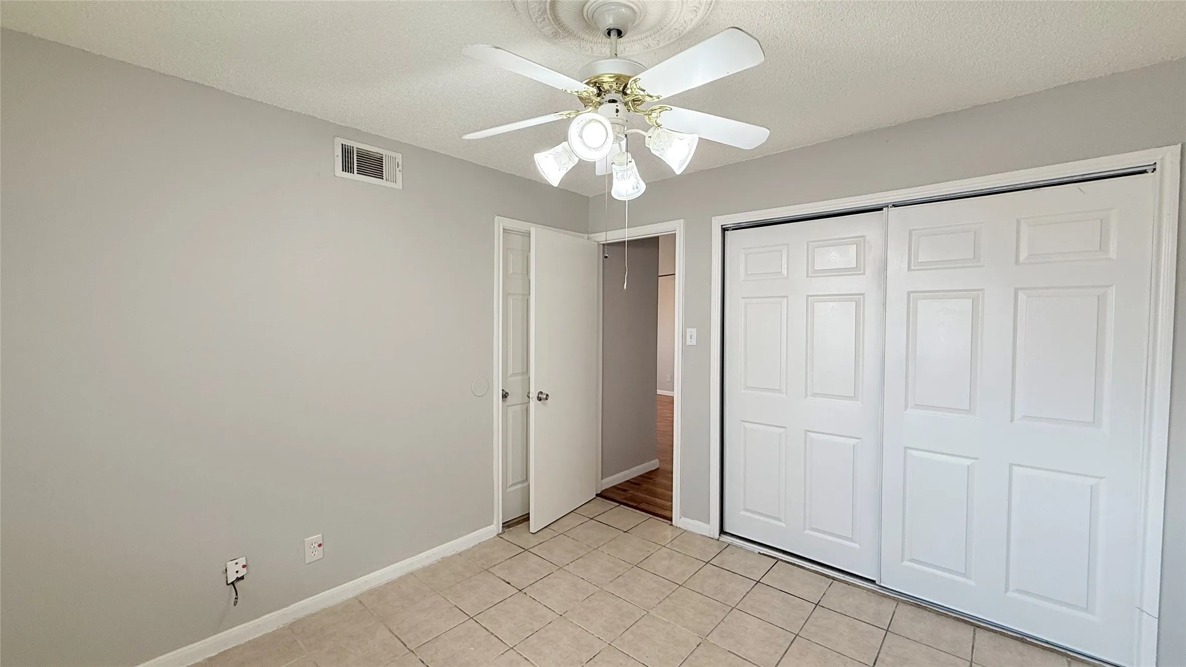 Recessed panel sliding closet doors, ceiling fan with light fixture, neutral paint, and square tile flooring
