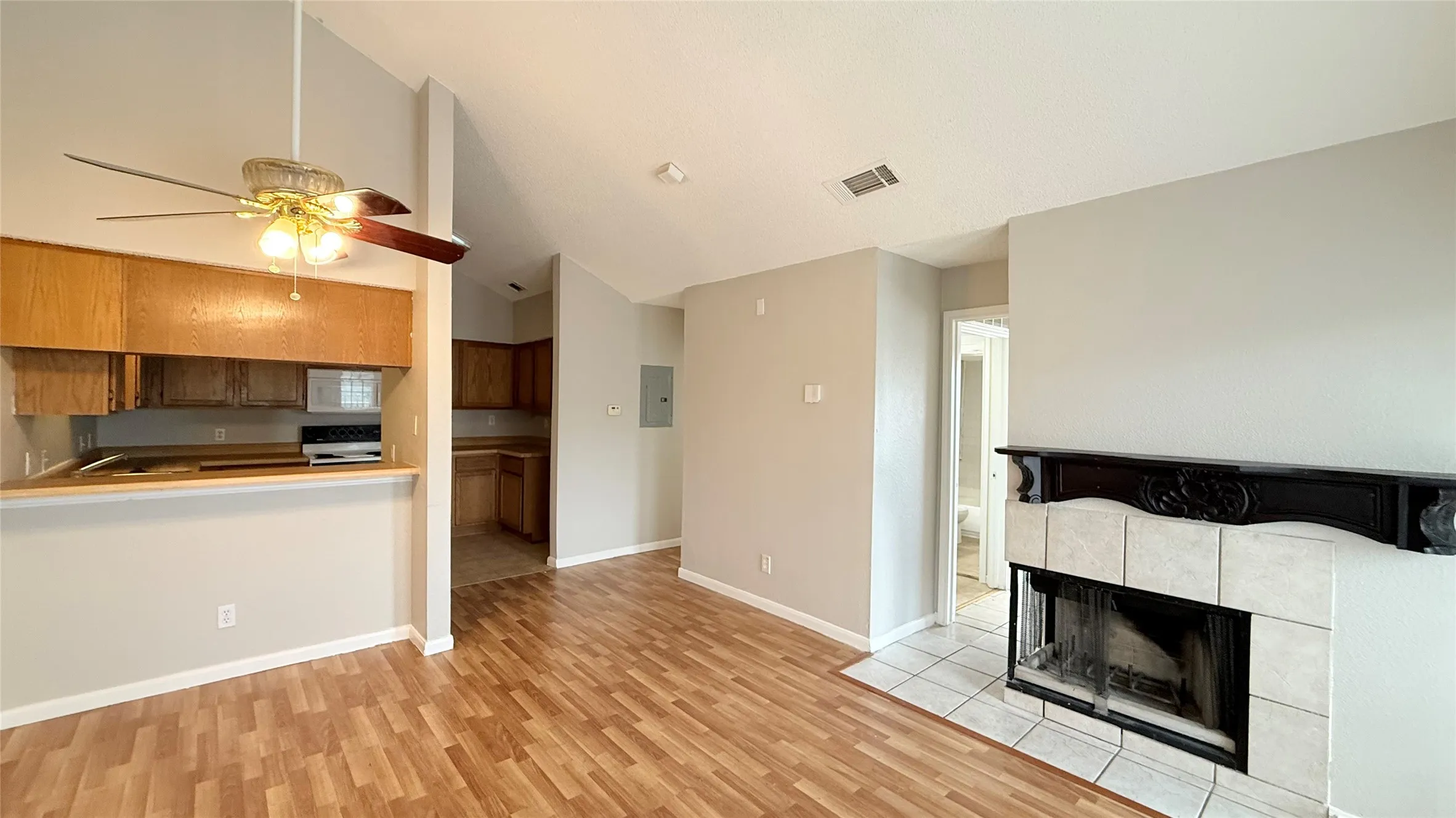 Wood-finish flooring, vaulted ceilings, and a fireplace with a decorative mantel and tile surround