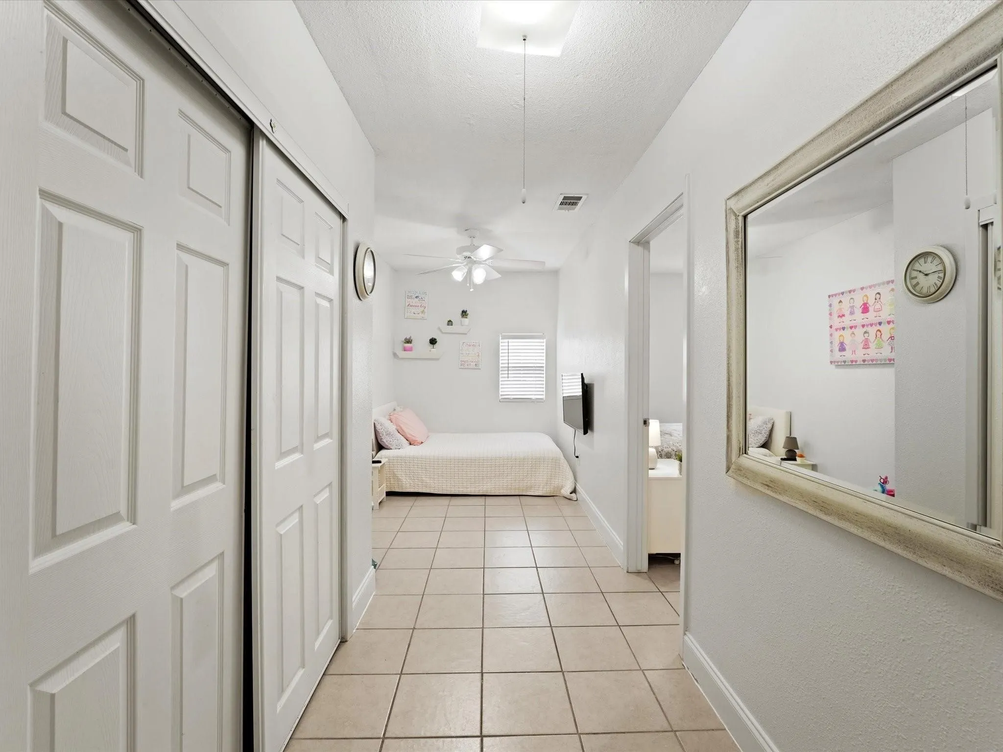 Hallway featuring neutral tile flooring, white walls, and a decorative mirror