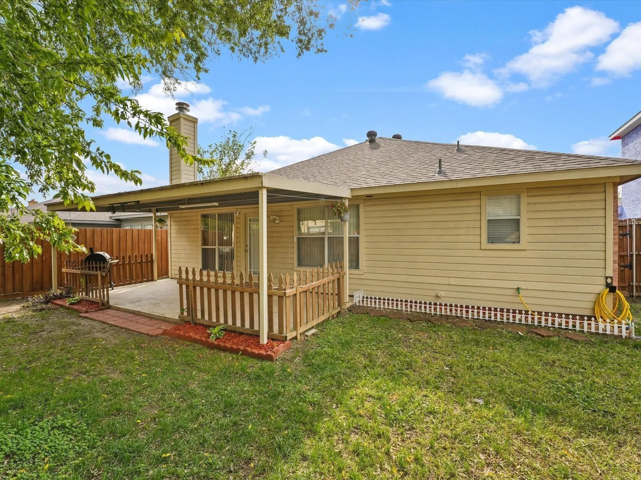 Expansive backyard featuring a covered patio, concrete surface, and wood picket fencing