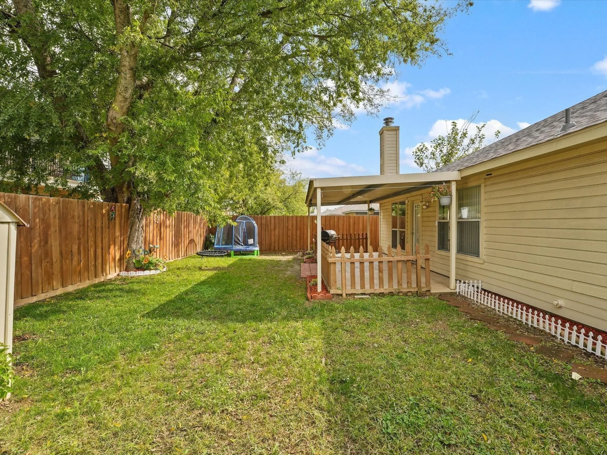Expansive backyard featuring a covered patio, wood privacy fencing, and mature trees