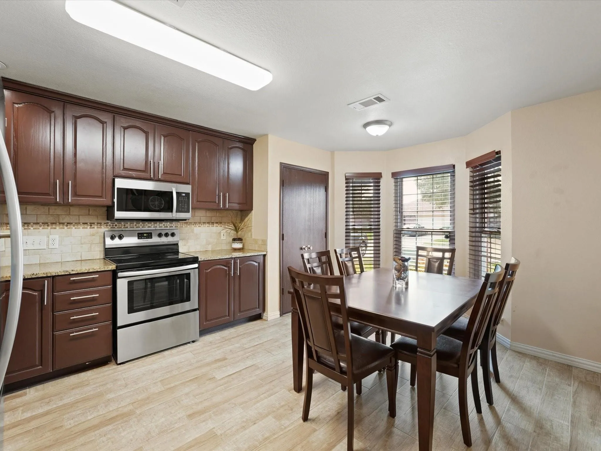 Kitchen with wood-finish flooring, stainless steel appliances, dark wood cabinetry, and granite countertops