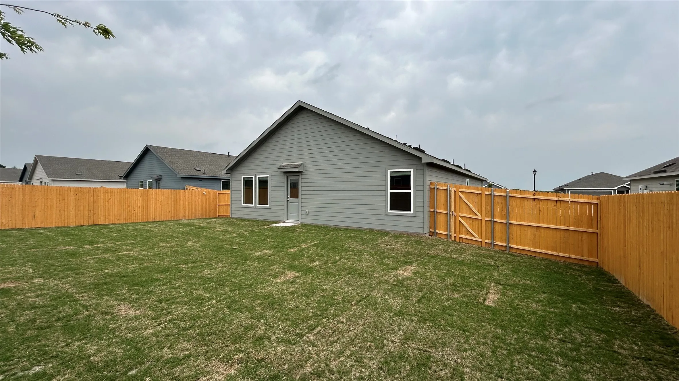 Expansive backyard featuring a new wood privacy fence, a wood gate, and a gray siding exterior