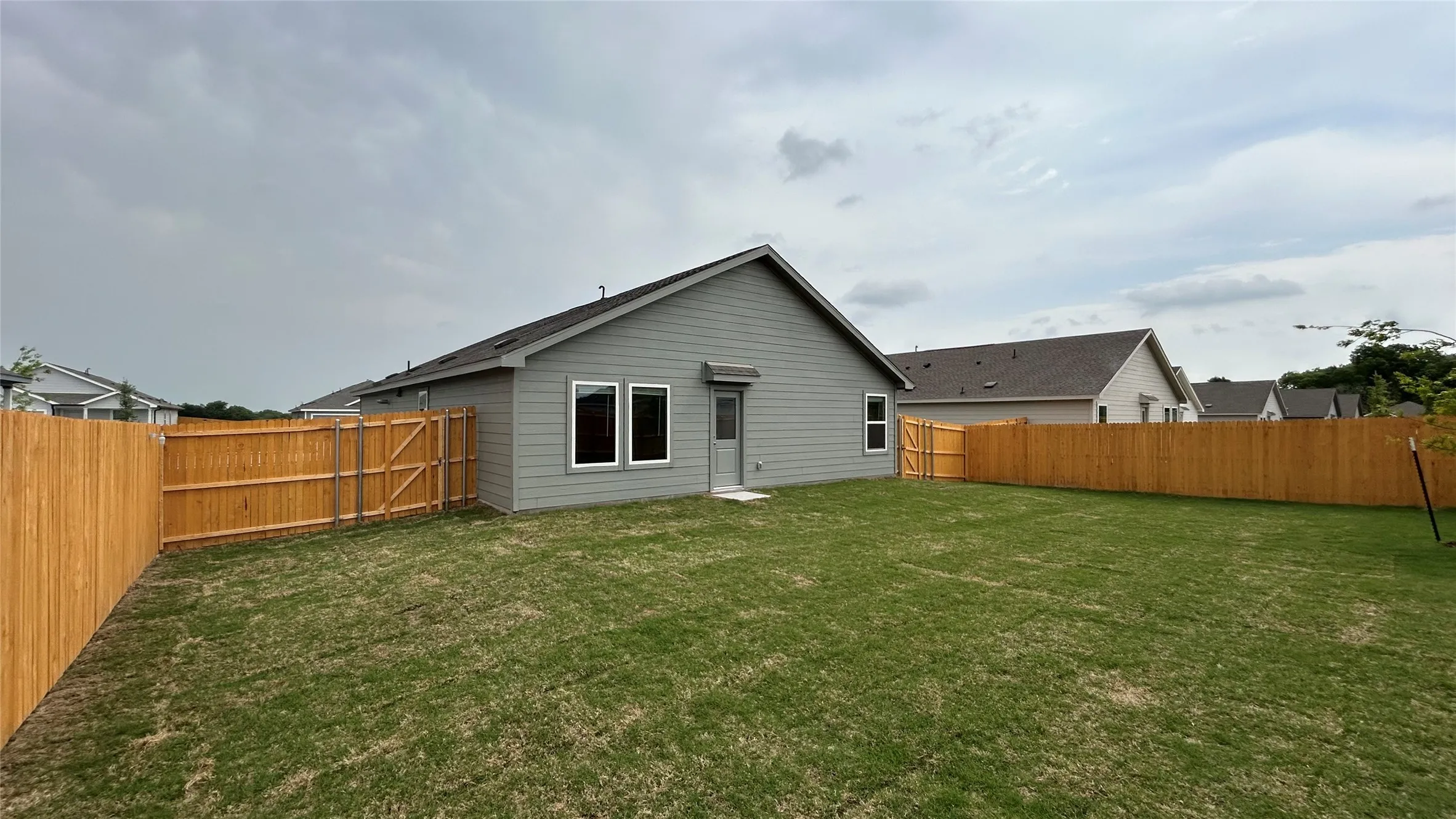 Expansive backyard with a manicured lawn, full wood fencing, and a side gate