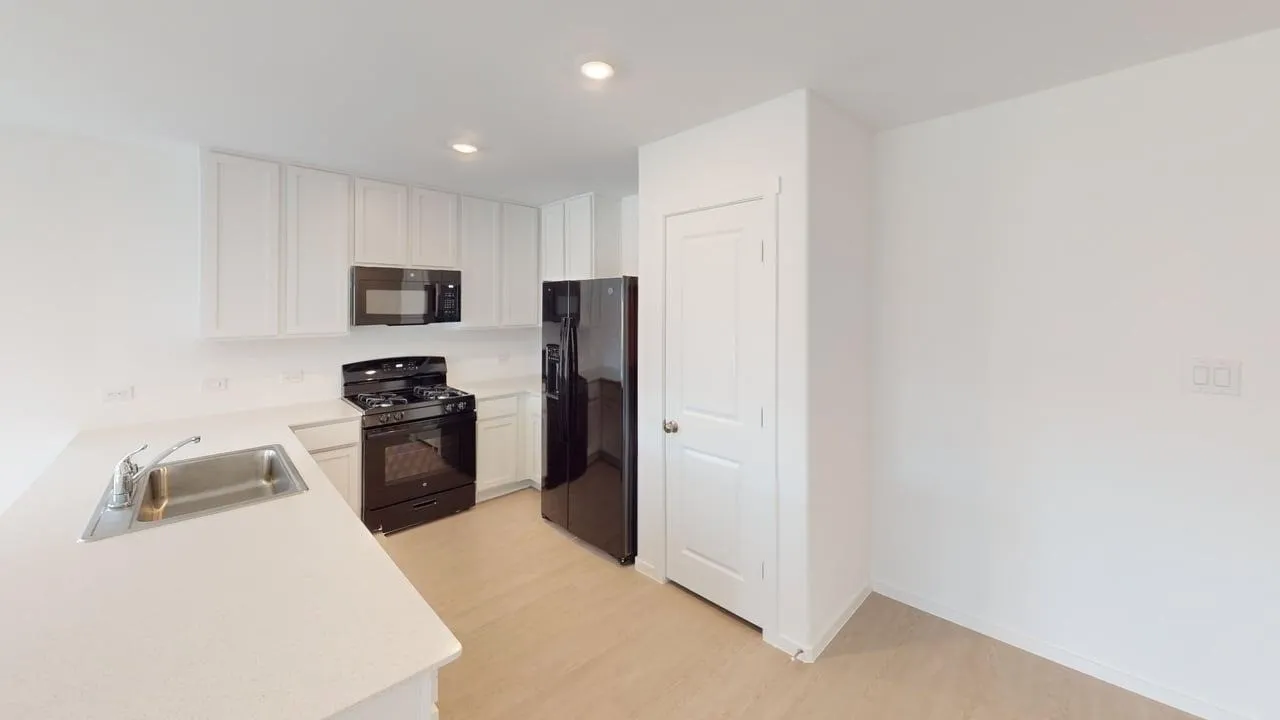 Kitchen featuring white cabinetry, light-toned countertops, a stainless steel sink with a chrome faucet, black appliances, and wood-finish flooring