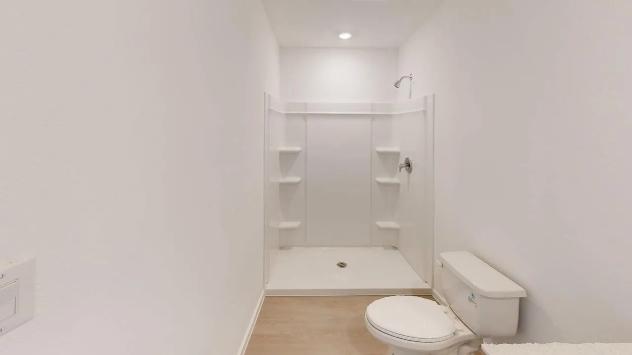 Shower stall with built-in shelving, chrome fixtures, and a flush toilet