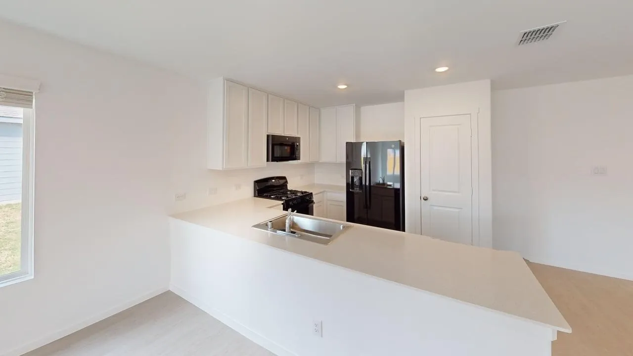 Kitchen featuring light-toned cabinetry, light countertops, integrated sink, and black appliances
