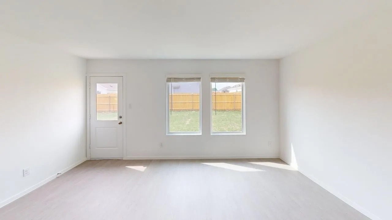 White interior walls, wood-finish flooring, two large windows, glass-paneled exterior door, and a fenced backyard