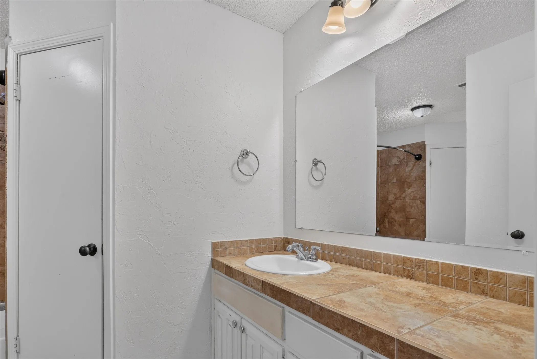 Vanity with an integrated sink, tile countertop, and mirror