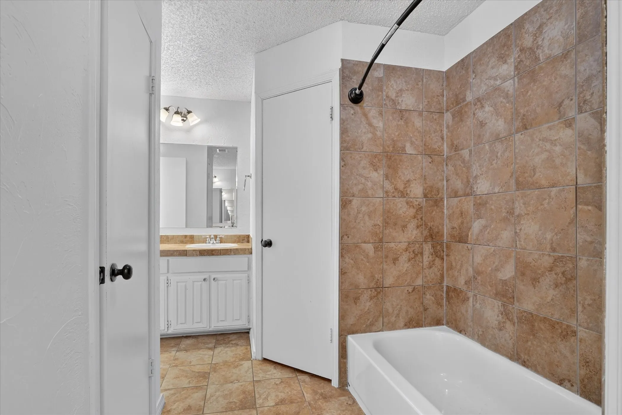 Bathroom featuring a white tub, tiled shower surround, and a vanity with a countertop and under-sink cabinetry