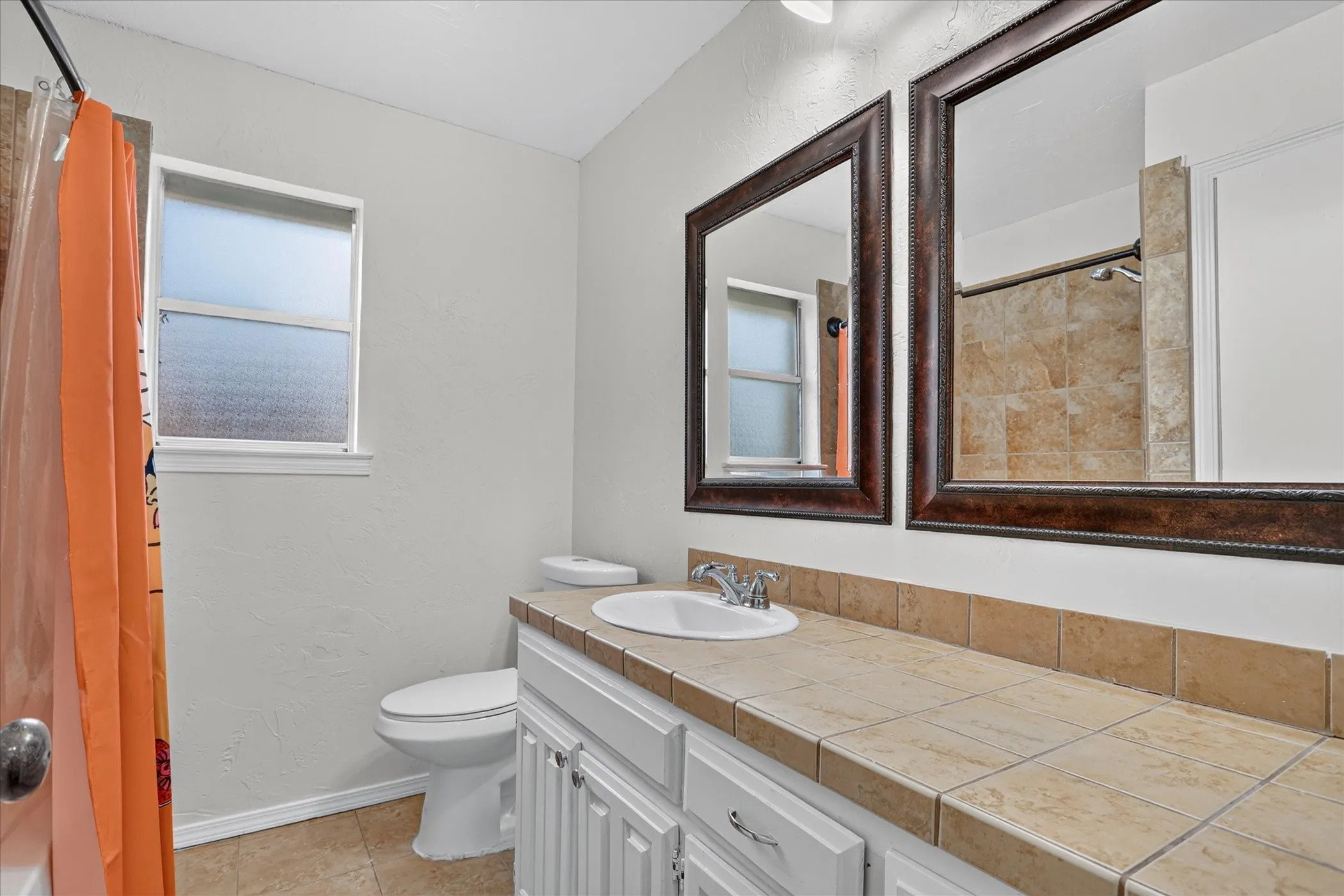 Bathroom featuring a tiled countertop, dual framed mirrors, and a window with privacy glass