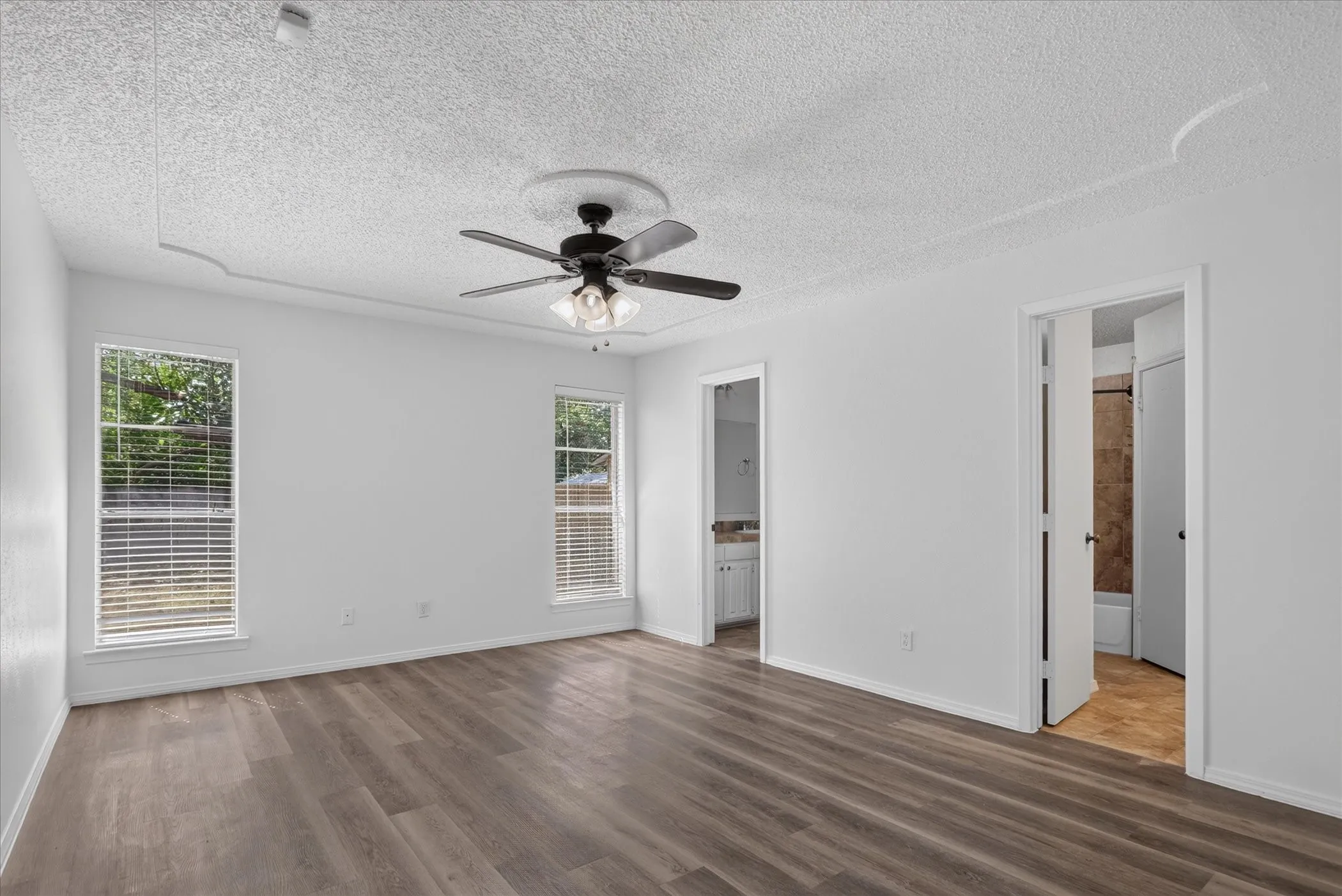 Wood-finish flooring, two windows with blinds, ceiling fan with integrated lighting, and two doorways
