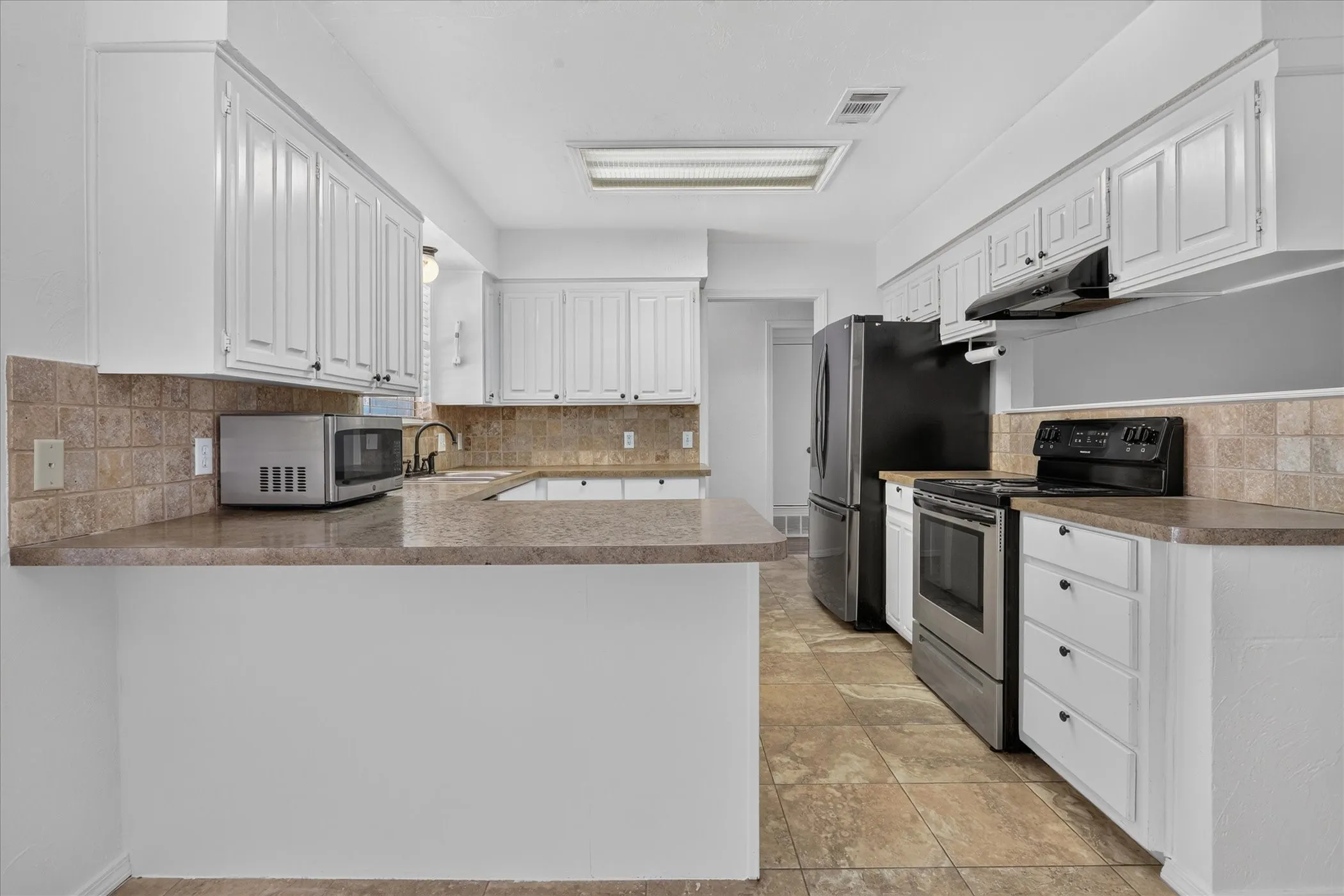 Kitchen featuring white cabinetry, tile flooring, stone-finish countertops, tiled backsplash, and stainless steel appliances