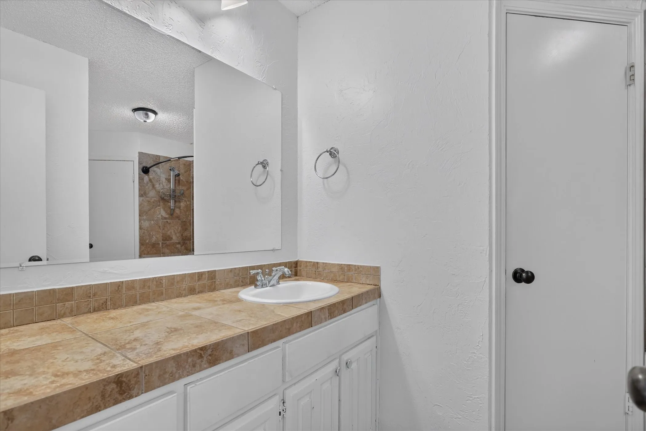 Vanity with a built-in sink, tile countertop, and white cabinetry