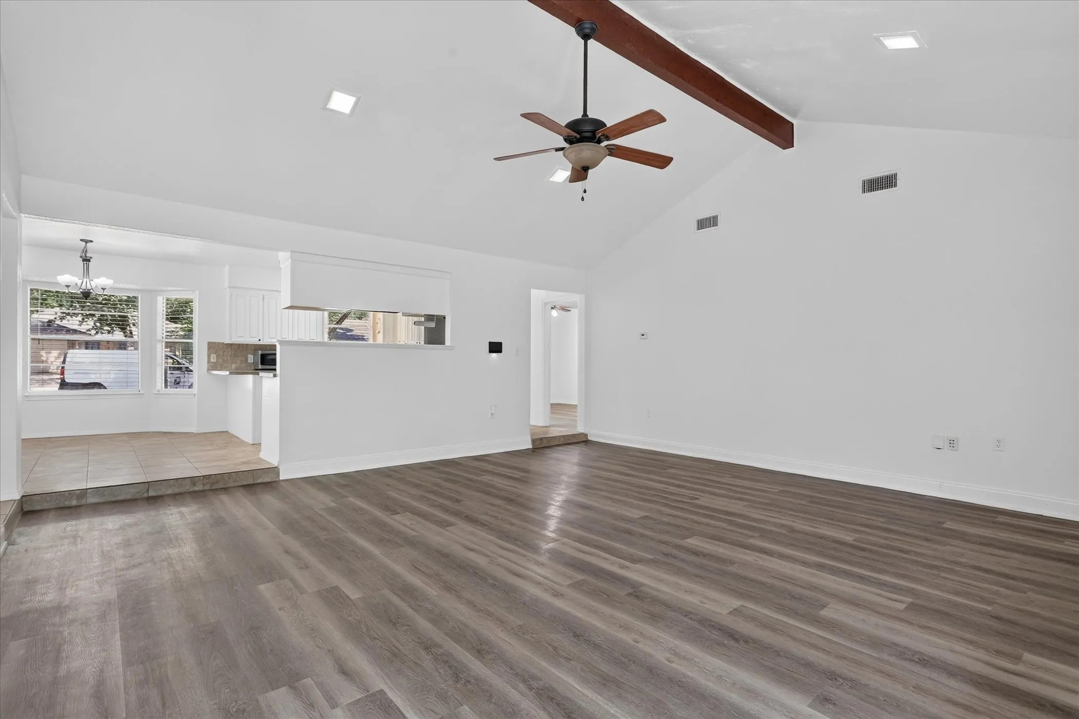 Vaulted ceiling with exposed wood beam, wood-finish flooring, recessed lighting, ceiling fan, and tiled dining area with dual windows
