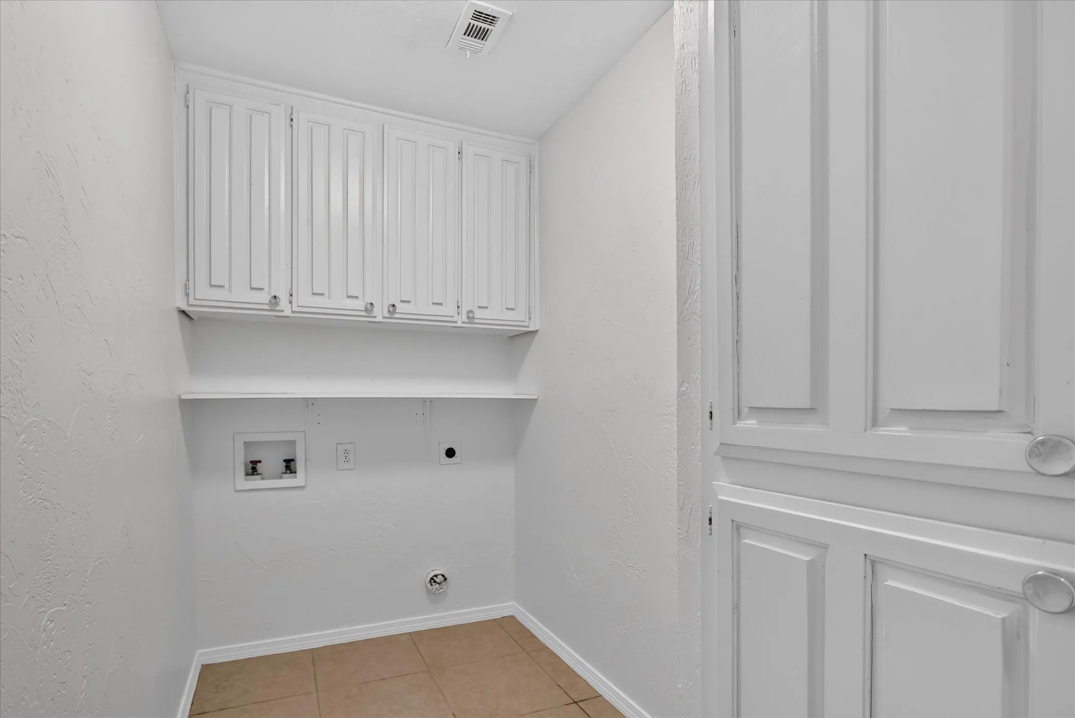White shaker-style cabinetry with silver hardware, an integrated wall shelf, and tile flooring