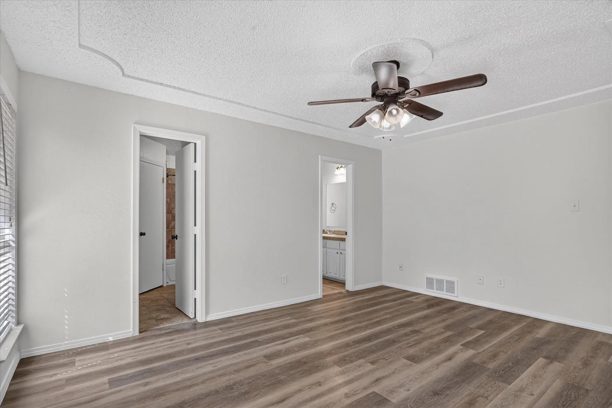 Wood-finish flooring, ceiling fan with integrated lighting, window with blinds, and white interior walls