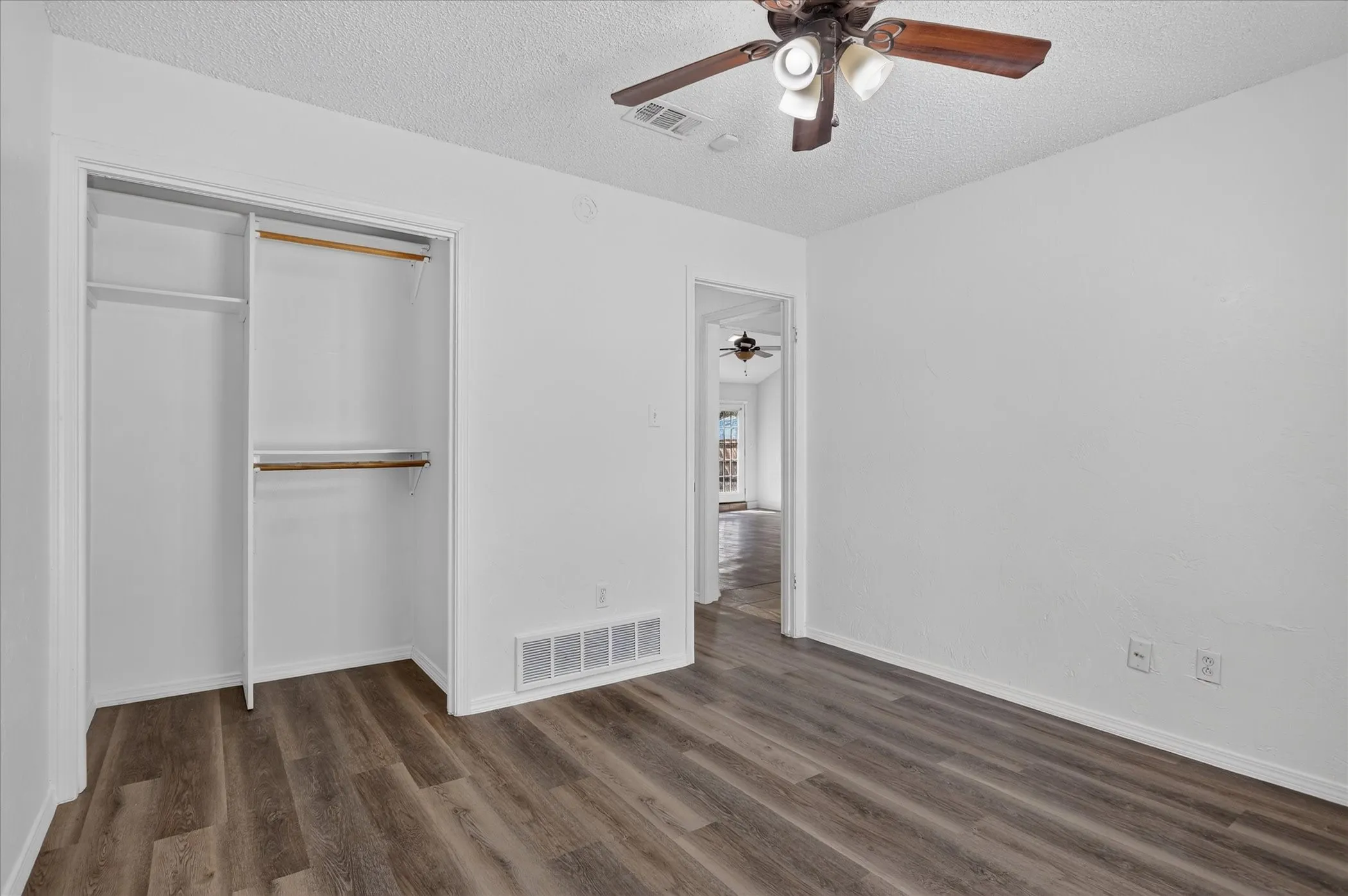 Wood-finish flooring, bright white walls, and a ceiling fan with integrated lighting
