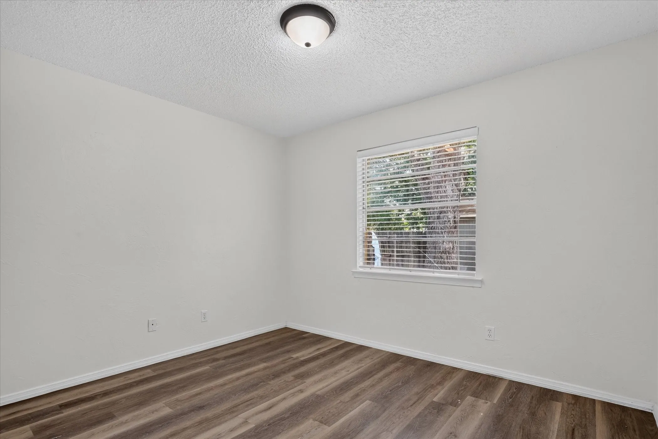 Wood-finish flooring, white walls, and a window with blinds