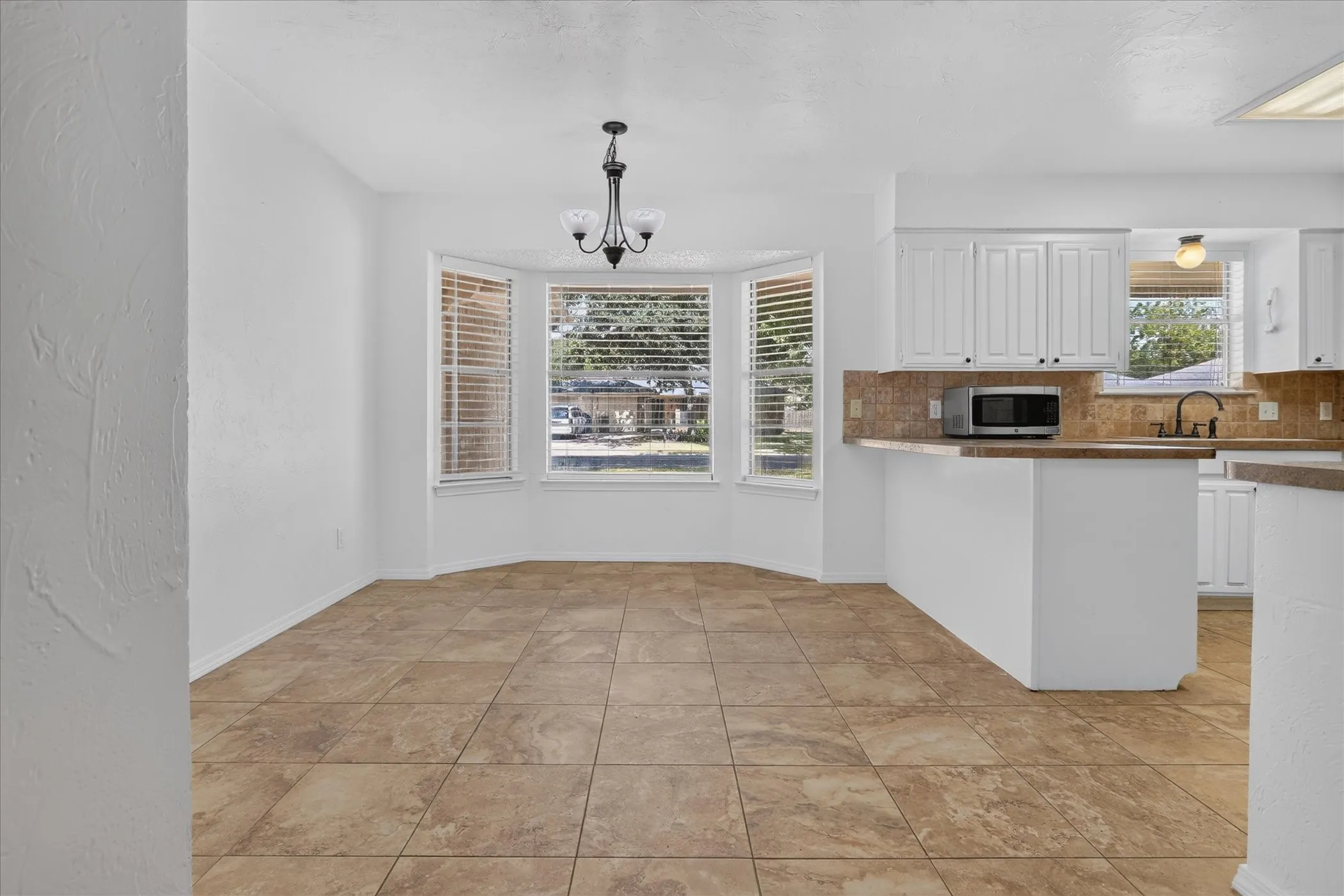 Bay window with blinds, tile flooring, white cabinetry, integrated microwave, and a black-finish faucet