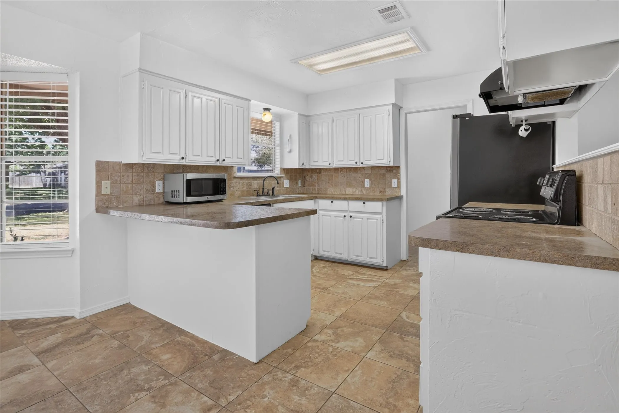 White cabinetry, tile flooring, brown countertops, and a tiled backsplash