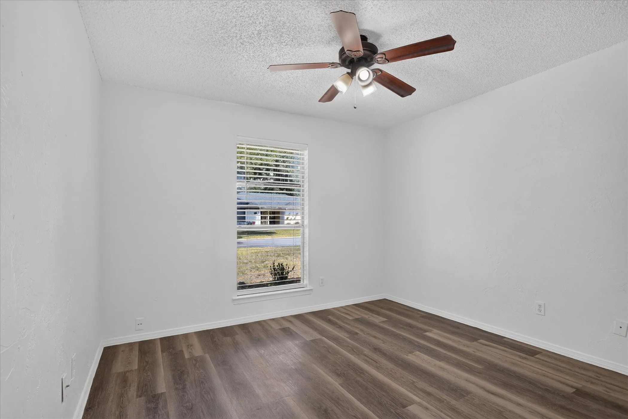 Wood-finish flooring, white painted walls, and a ceiling fan with integrated lighting