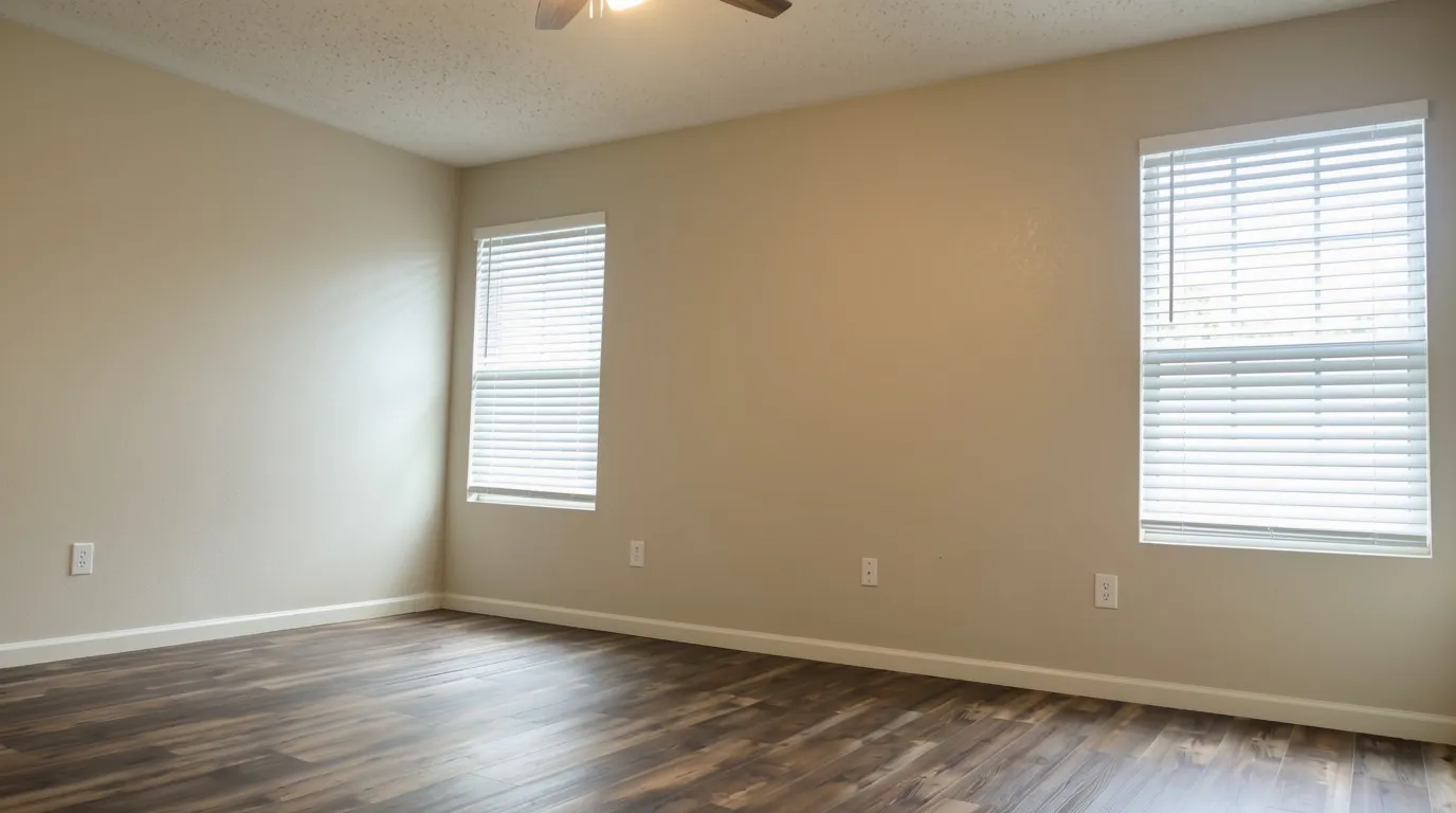 Spacious room featuring wood-finish flooring and two windows with blinds